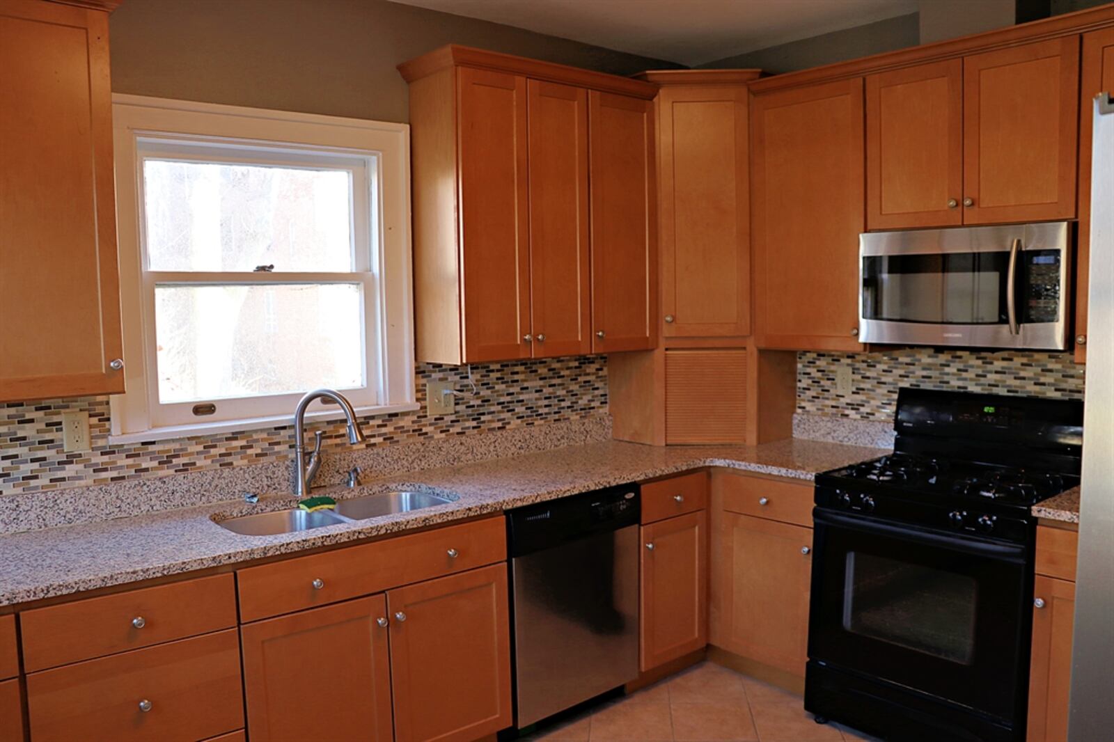 Hickory cabinetry is complemented by granite counters within the updated kitchen. A window is above the sink and cabinetry includes an appliance garage. Mosaic-tile backsplash fills all the wall space between counters and cabinets, and the kitchen has ceramic-tile flooring.