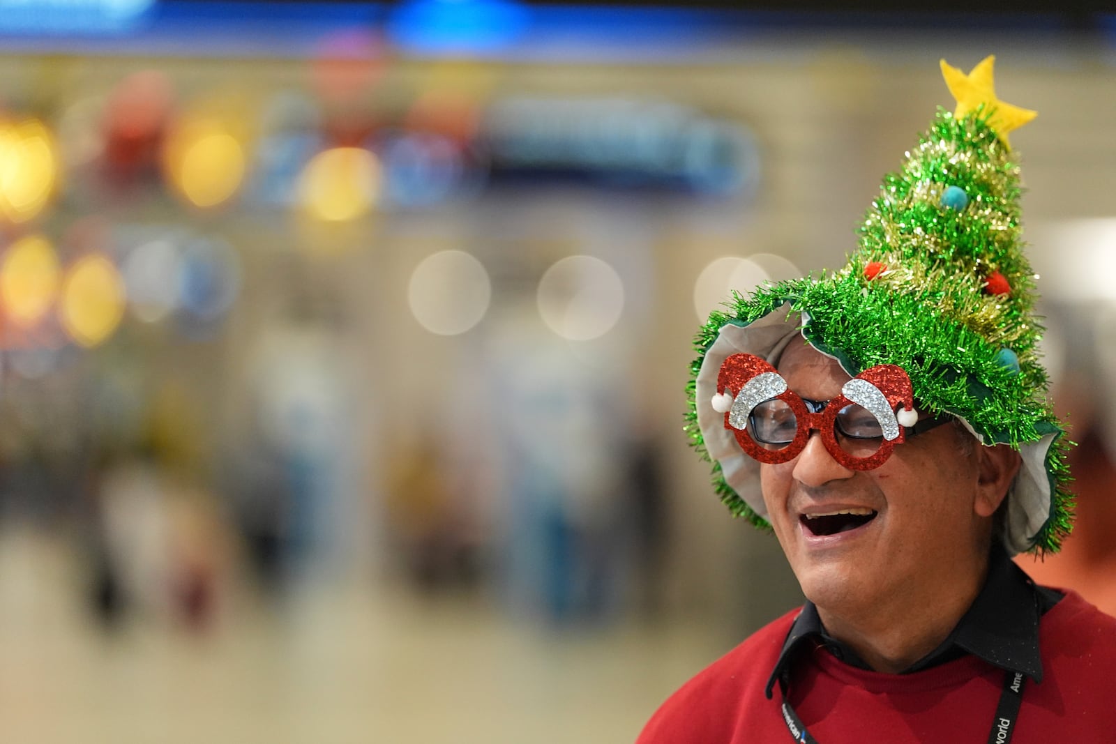 Cesar Davila, who works for the American Airlines partner providing wheelchair assistance, wears a Christmas tree hat and festive glasses as he waits for a traveler to help inside the American Airlines terminal at Miami International Airport, on Christmas Eve, Tuesday, Dec. 24, 2024, in Miami. (AP Photo/Rebecca Blackwell)