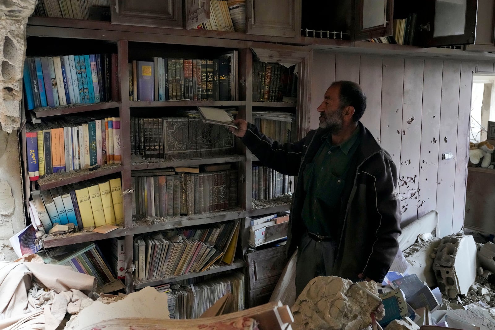 A resident checks a library in a damaged house, in Baalbek, eastern Lebanon, Thursday, Nov. 28, 2024. (AP Photo/Hassan Ammar)