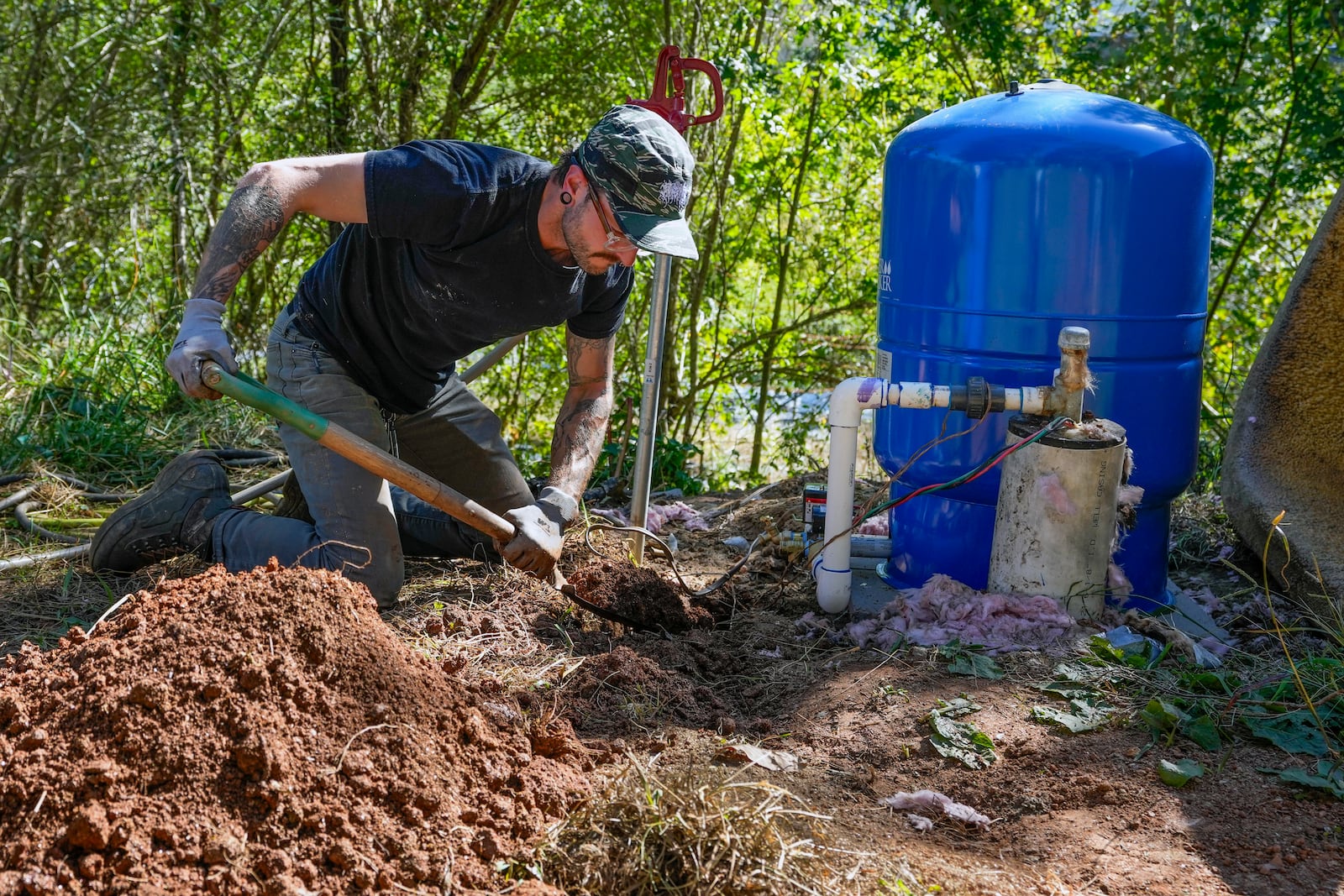 Volunteer, Anthony Rubino digs a ditch for pipes to connect water from a community well that will more easily provide the neighborhood with water, Monday, Oct. 14, 2024, in Asheville, N.C. (AP Photo/Kathy Kmonicek)