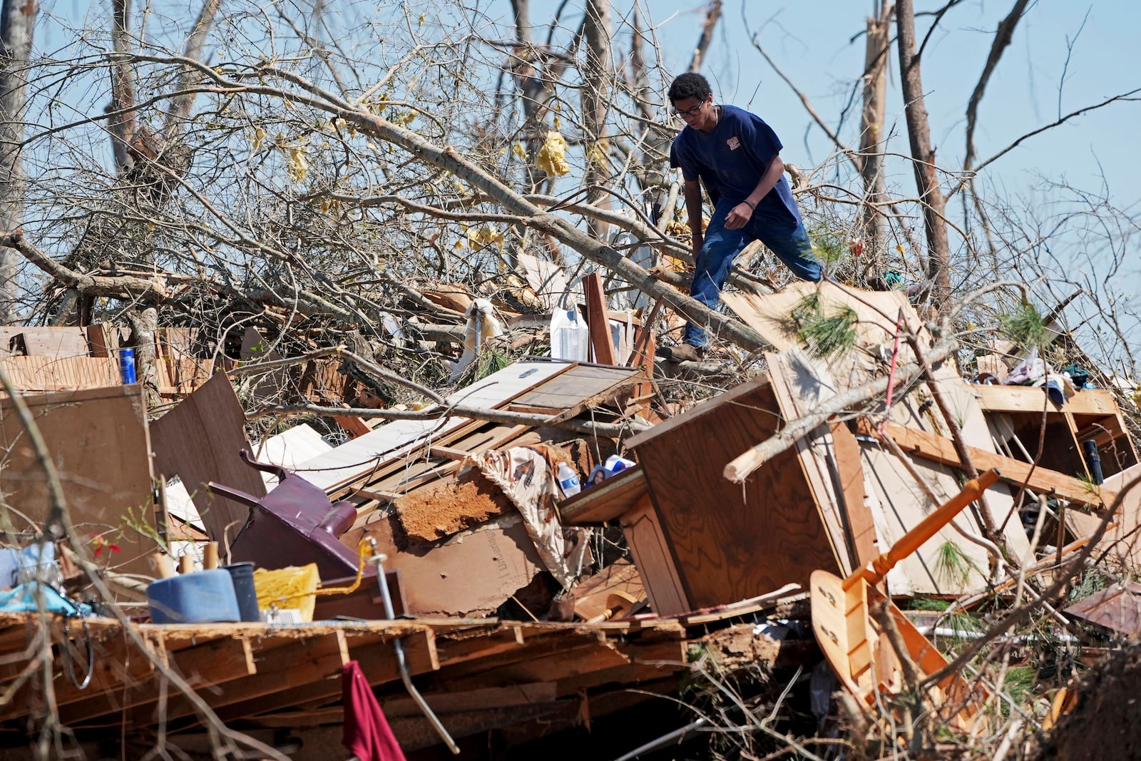 Family friend Trey Bridges, 16, climbs a mountain of tornado debris to help the Blansett family recover items not destroyed by Saturday's tornado, Sunday, March 16, 2025, in Tylertown, Miss. (AP Photo/Rogelio V. Solis)