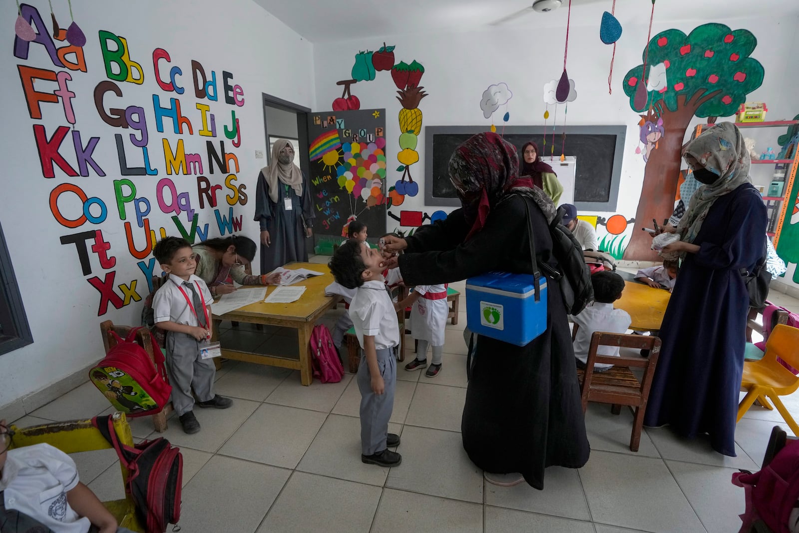 A health worker, center, administers a polio vaccine to a child in a school, in Karachi, Pakistan, Monday, Oct. 28, 2024. (AP Photo/Fareed Khan)