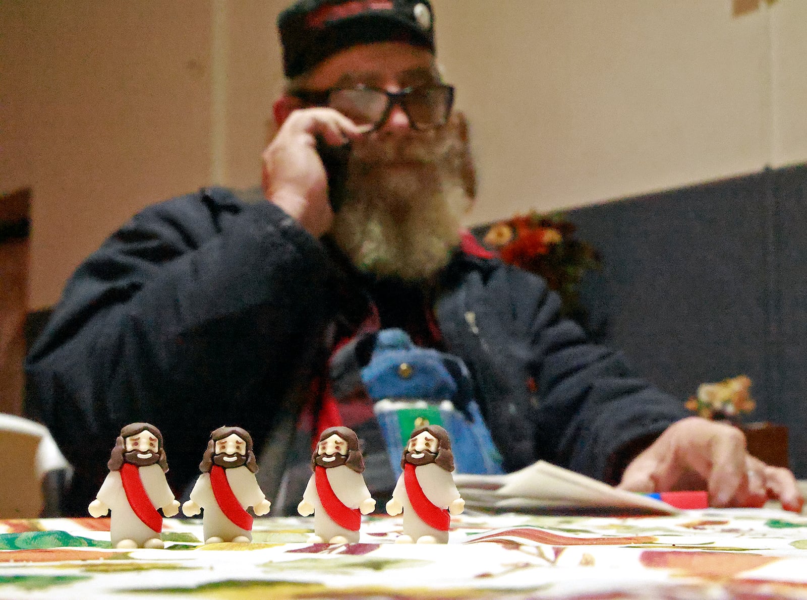 Four tiny Jesus figures are lined up as Kenneth "Barron" Seelig talks to a volunteer on the phone about dinner Tuesday night at the warming shelter Seelig organized and opened with help of volunteers in the gymnasium of the Victory Faith Center. Seelig carries several of the tiny Jesus figures with him at all times to give out. BILL LACKEY/STAFF