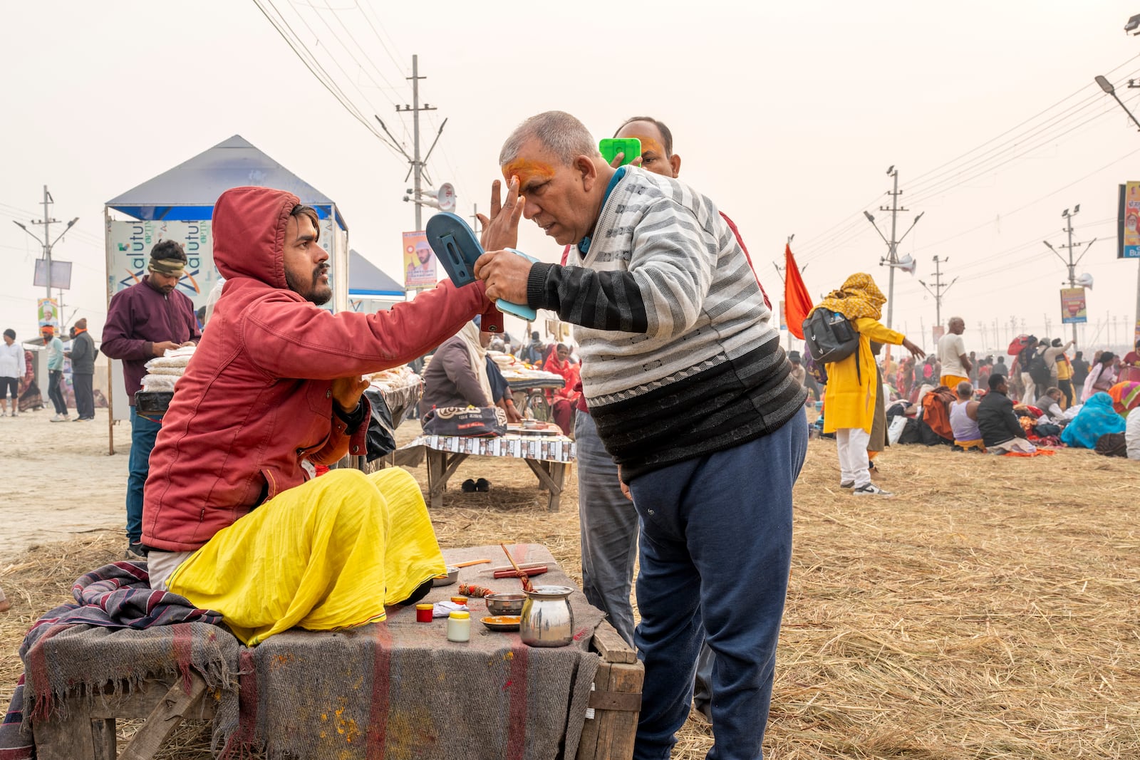 A Hindu devotee looks into a mirror as he gets his forehead smeared by a holy man at the confluence of the Ganges, the Yamuna and the mythical Saraswati rivers, a day before the official beginning of the 45-day-long Maha Kumbh festival, in Prayagraj, India, Sunday, Jan. 12, 2025. (AP Photo/Ashwini Bhatia)