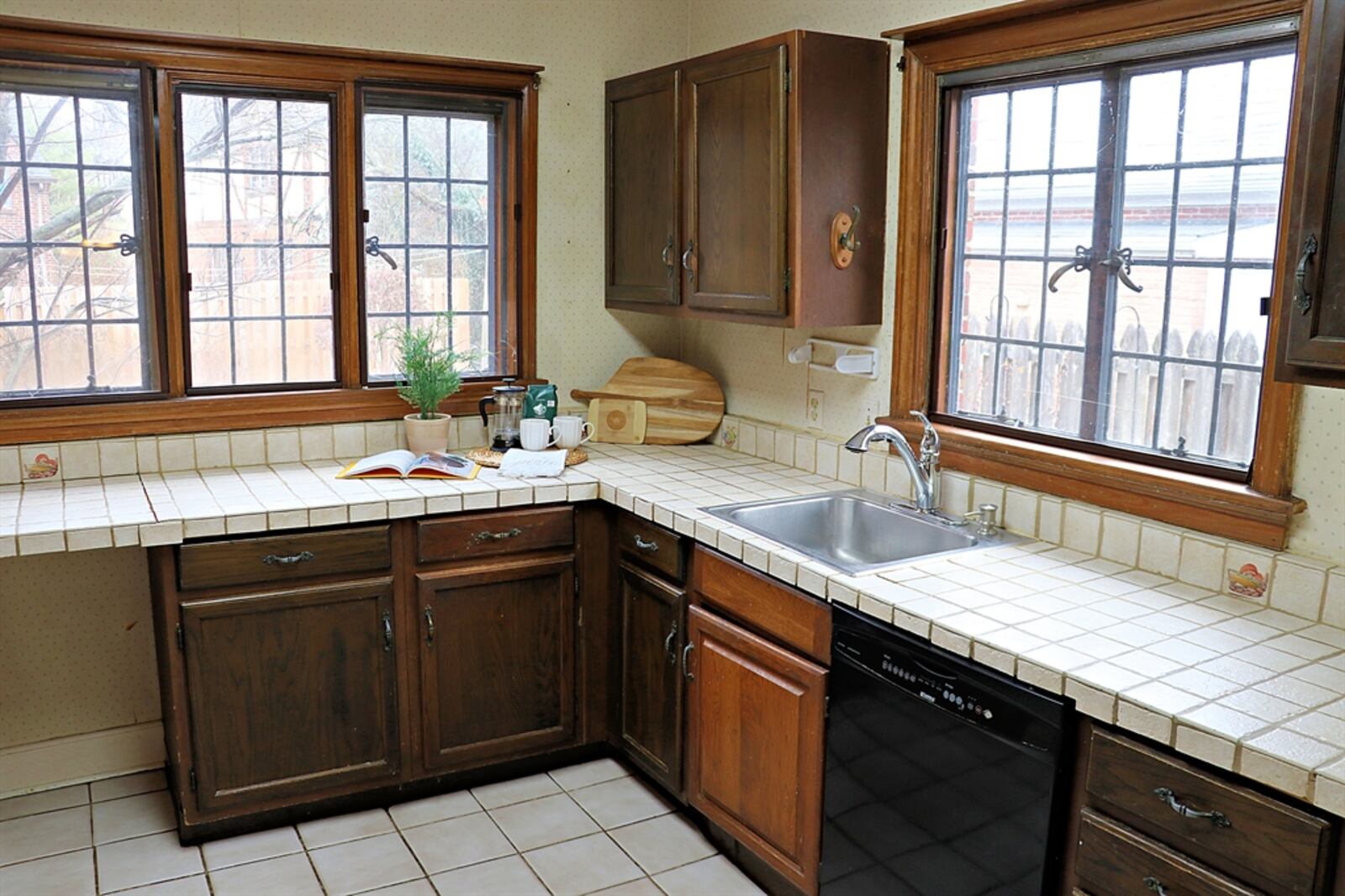 Ceramic-tile counters complement the dark cabinetry that fills three walls of the kitchen. The sink is below a window, and triple windows fill a preparation area with natural light. 