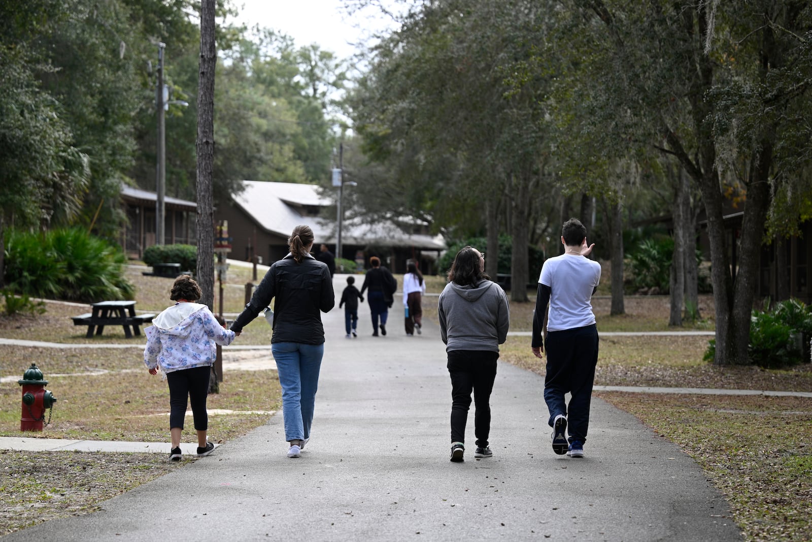 Families and volunteer counselors past cabins at Camp Boggy Creek, where children with serious illnesses and their families are provided with a free camp experience, Saturday, Jan. 11, 2025, in Eustis, Fla. (AP Photo/Phelan M. Ebenhack)