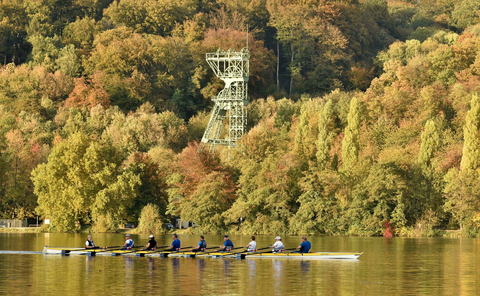 FILE - People row on the Lake Baldeney in front of an old headframe of a former coal mine in the warm autumn sun in Essen, Germany, Tuesday, Oct. 16, 2018. (AP Photo/Martin Meissner, File)