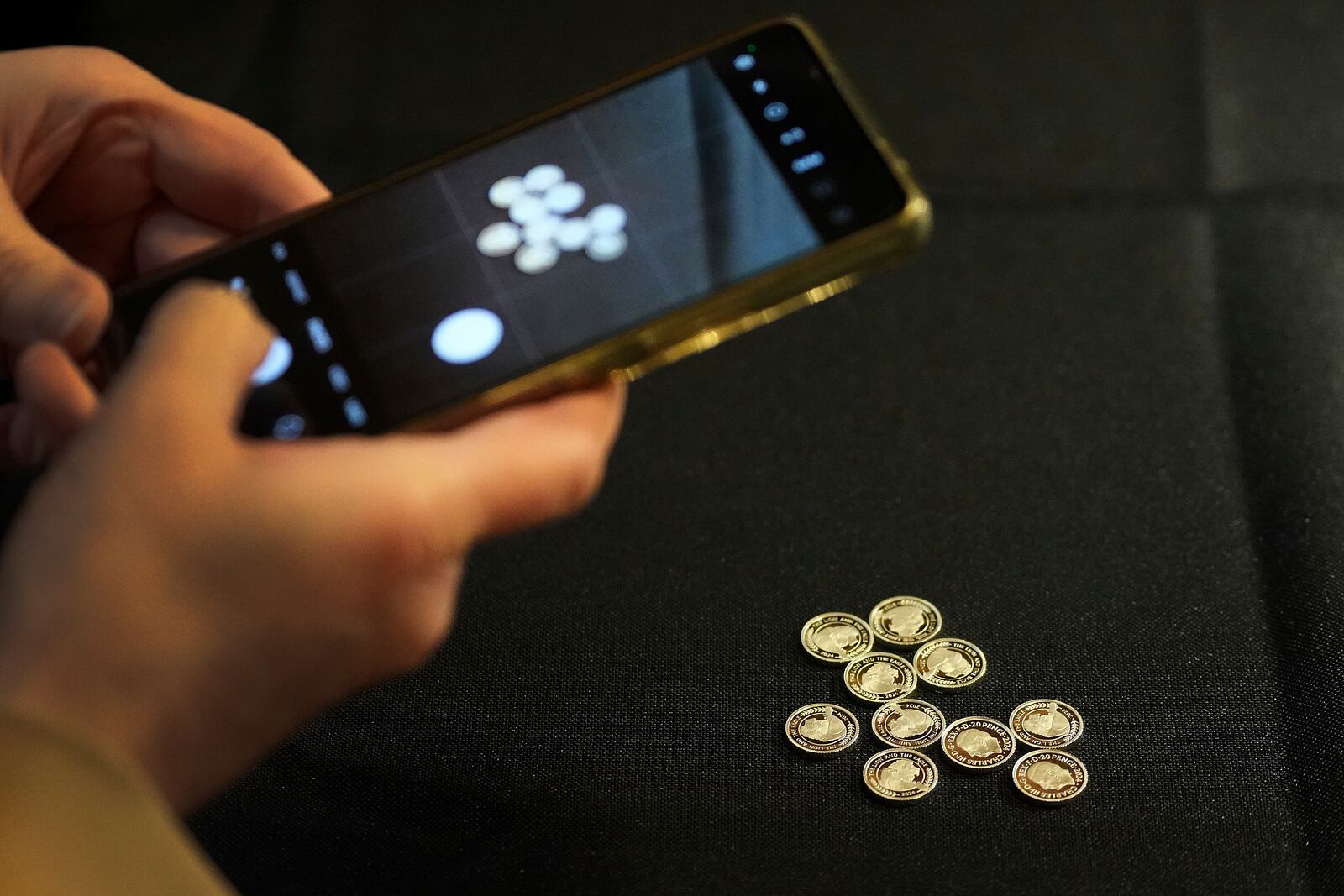 A visitor takkes a picture of small coins on her phones during the "Trial of the Pyx,'' a ceremony that dates to the 12th Century in which coins are weighed in order to make certain they are up to standard, at the Goldsmiths' Hall in London, Tuesday, Feb. 11, 2025.(AP Photo/Frank Augstein)