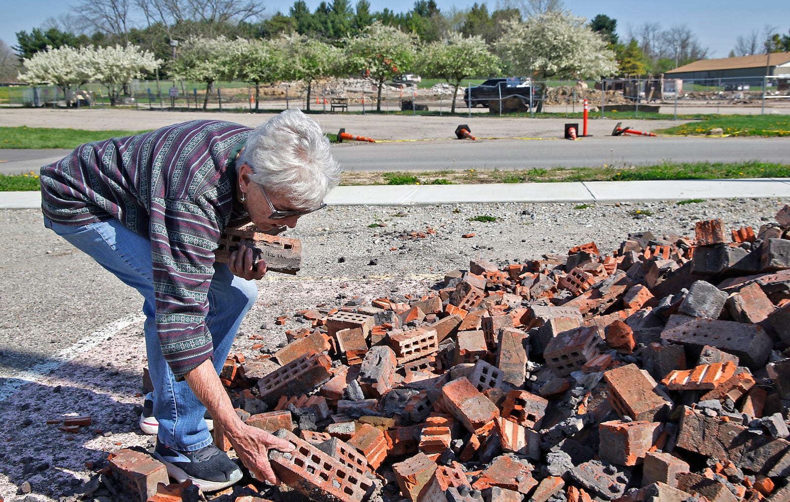 Karen Clingman collects bricks from the old Kenton Ridge High School for her son Monday, April 15, 2024. The high school, which used to be located in the background, was recently demolished and bricks from the building were piled in the parking lot for people to save as keepsakes. A new combined Kenton Ridge School was opened at the beginning of this school year. BILL LACKEY/STAFF