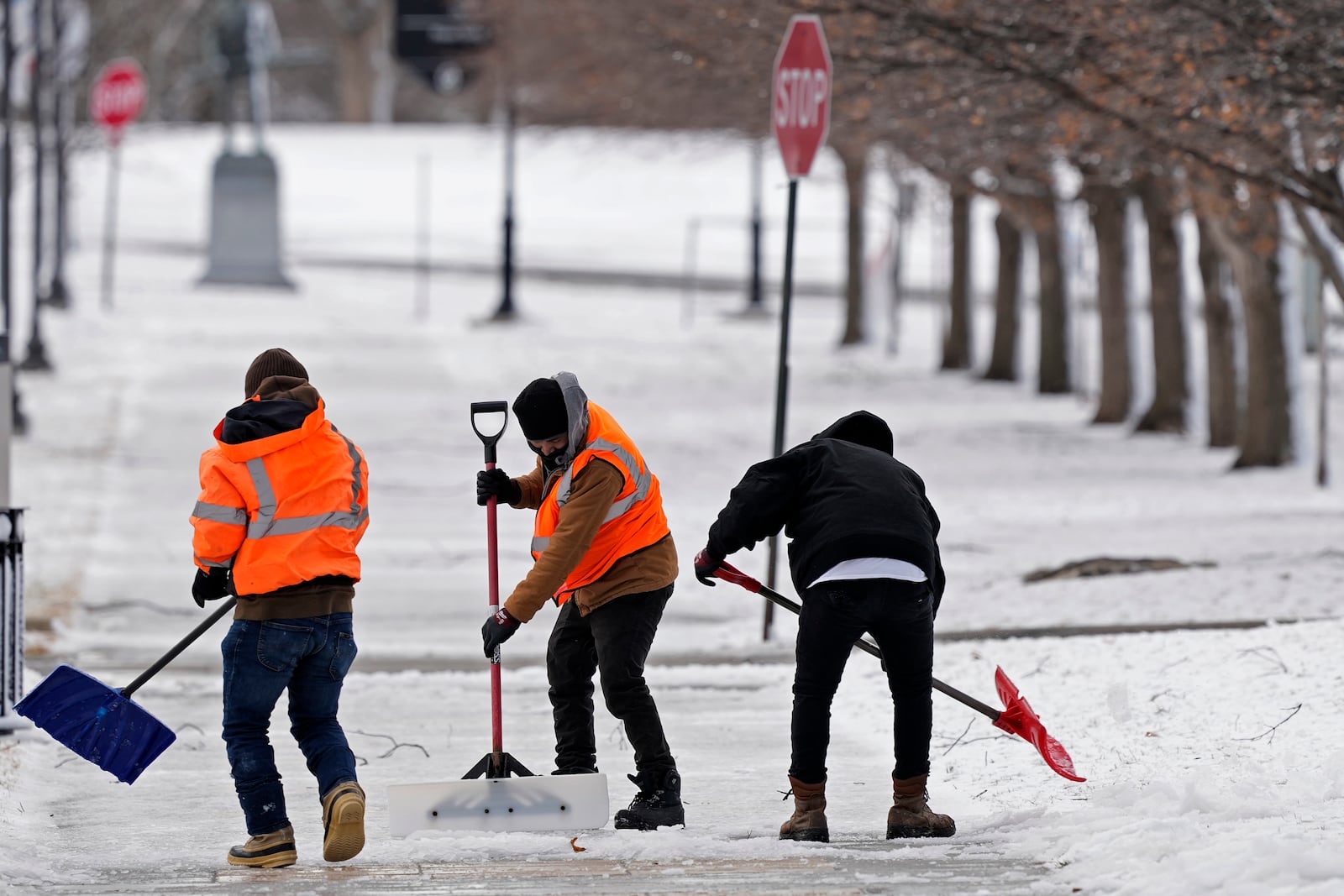 Workers clear a layer of ice from a sidewalk at the Liberty Memorial after a winter storm passed through the area overnight, Wednesday, March 5, 2025, in Kansas City, Mo. (AP Photo/Charlie Riedel)