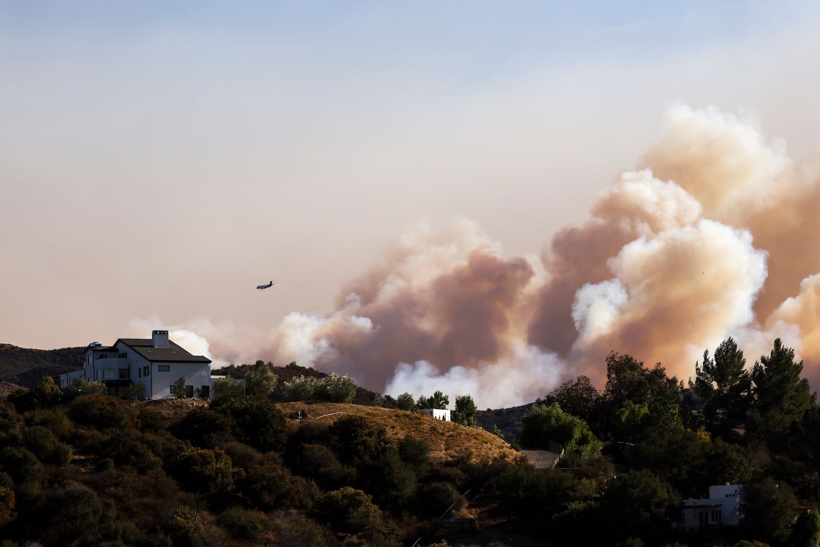 A firefighting plane makes drops over ridges as the Palisades Fire burns in the hills between Pacific Palisades and Malibu Wednesday, Jan. 8, 2025 in Topanga, Calif. (AP Photo/Etienne Laurent)