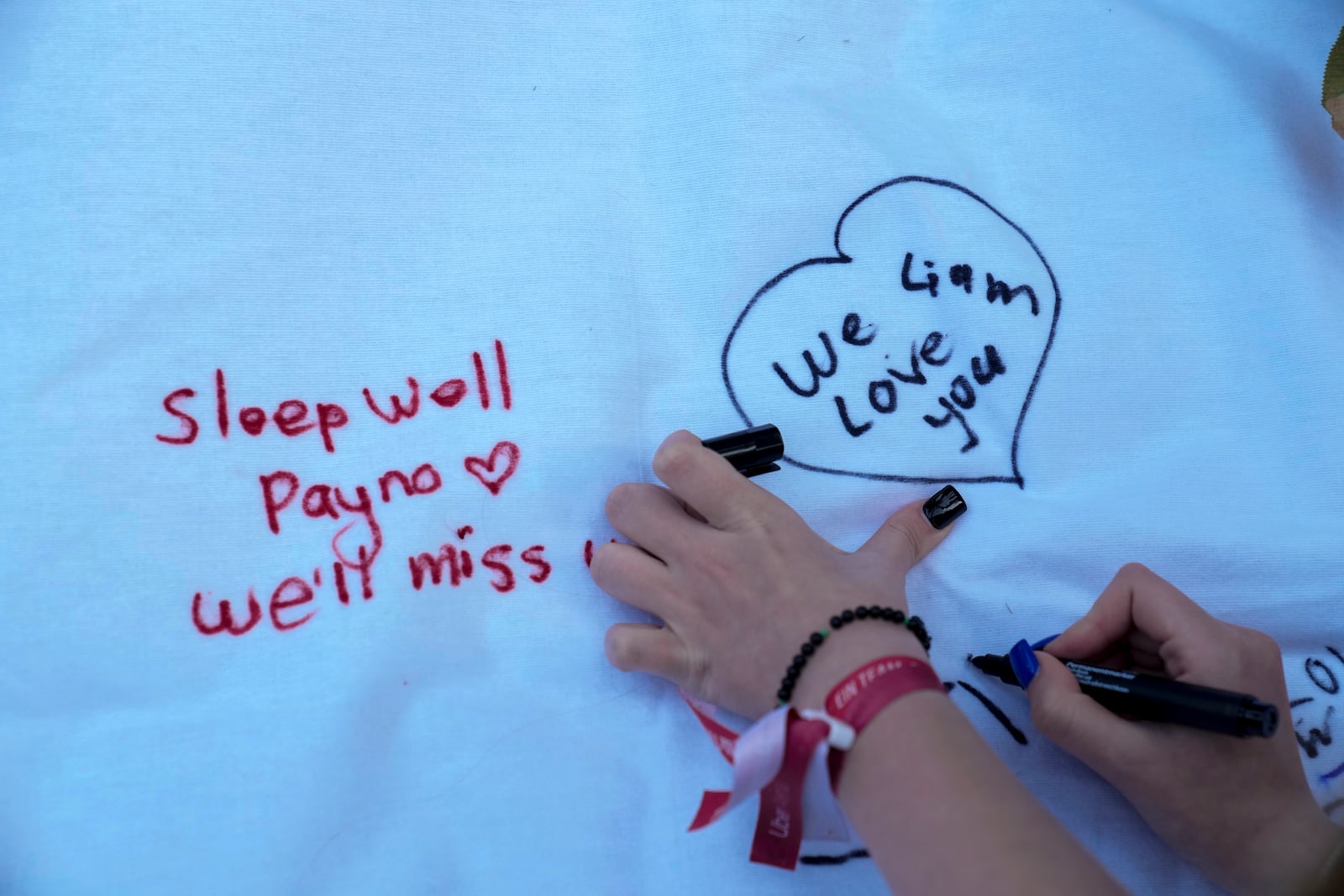 A female writes a message as fans gather to pay tribute to late British singer Liam Payne, former member of the British pop band One Direction in Treptower Park in Berlin, Germany, Sunday, Oct. 20, 2024. (AP Photo/Ebrahim Noroozi)