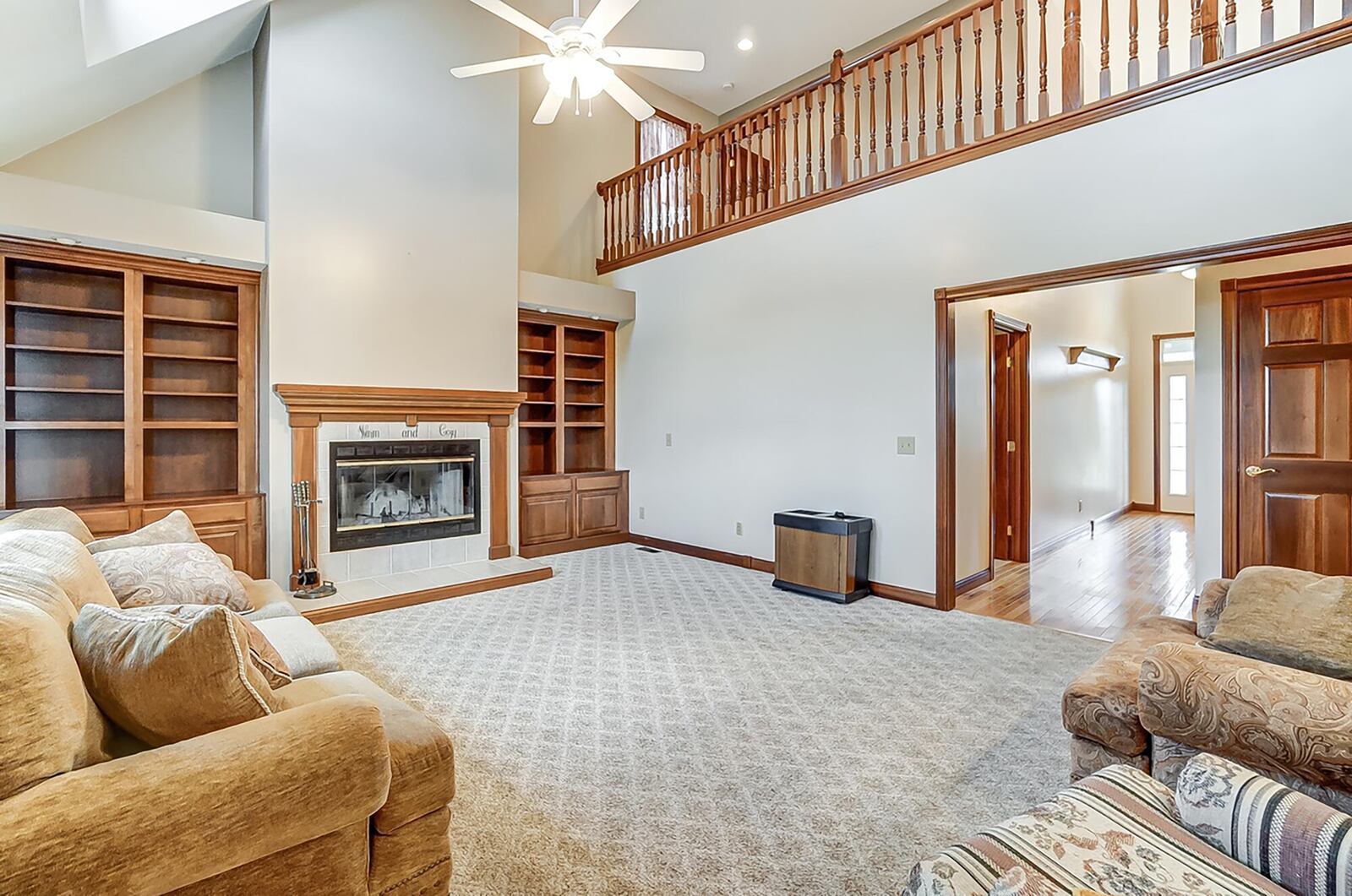 The two story great room has a wood burning fireplace, built in bookcases, a ceiling fan and two dormer windows near the ceiling.