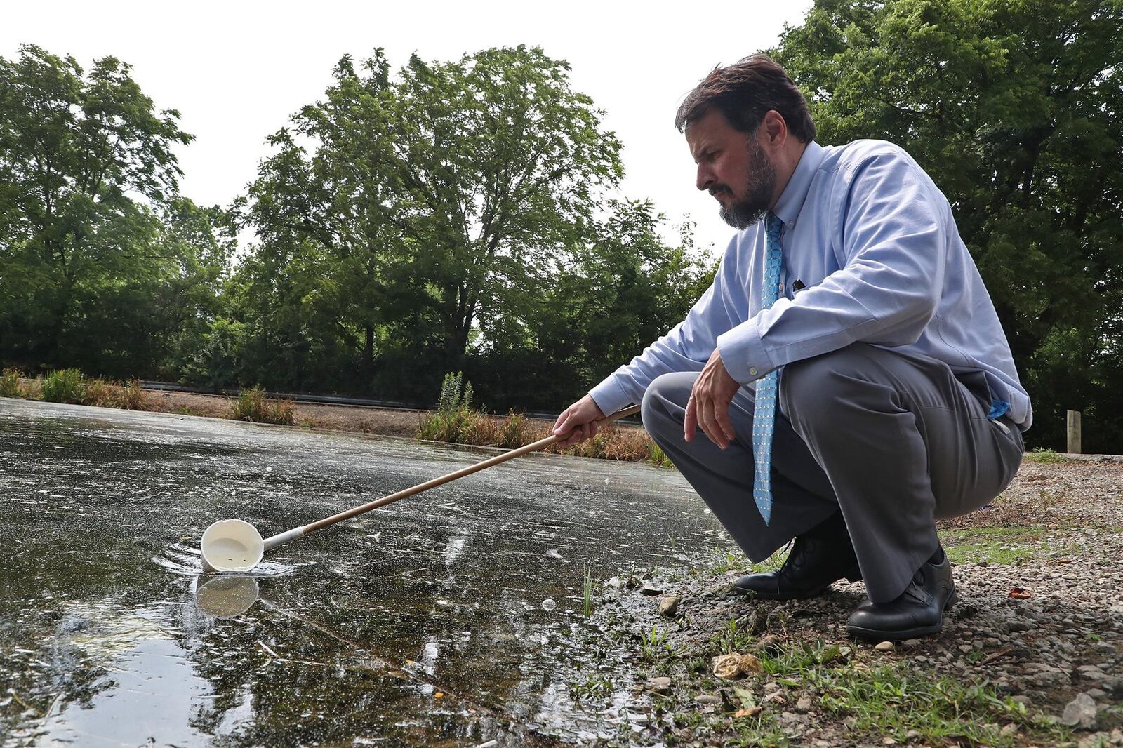 Larry Shaffer, the director of Environment Health at the Clark County Combined Health District, skims the top of the water at Old Reid Park as he looks for mosquito larvae in July 2020. BILL LACKEY/STAFF