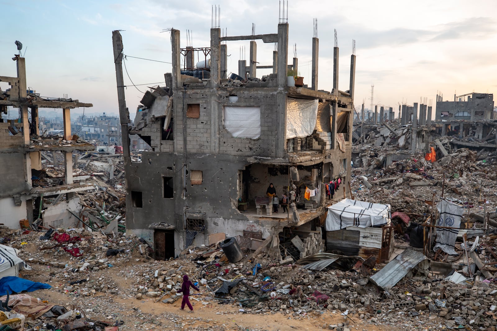 Palestinians stand in their partially standing homes, covered with sheets as makeshift walls, in an area largely destroyed by the Israeli army's air and ground offensive in Jabaliya, Gaza Strip, on Tuesday, Feb. 11, 2025. (AP Photo/Jehad Alshrafi)