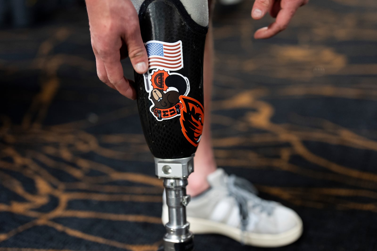 Ukrainian veteran Stanislav Povkhan places an American flag sticker on his prosthetic leg after a lesson with Oregon Adaptive Sports on the three track skiing method at Hoodoo Ski Area in central Oregon on Thursday, March 6, 2025. (AP Photo/Jenny Kane)