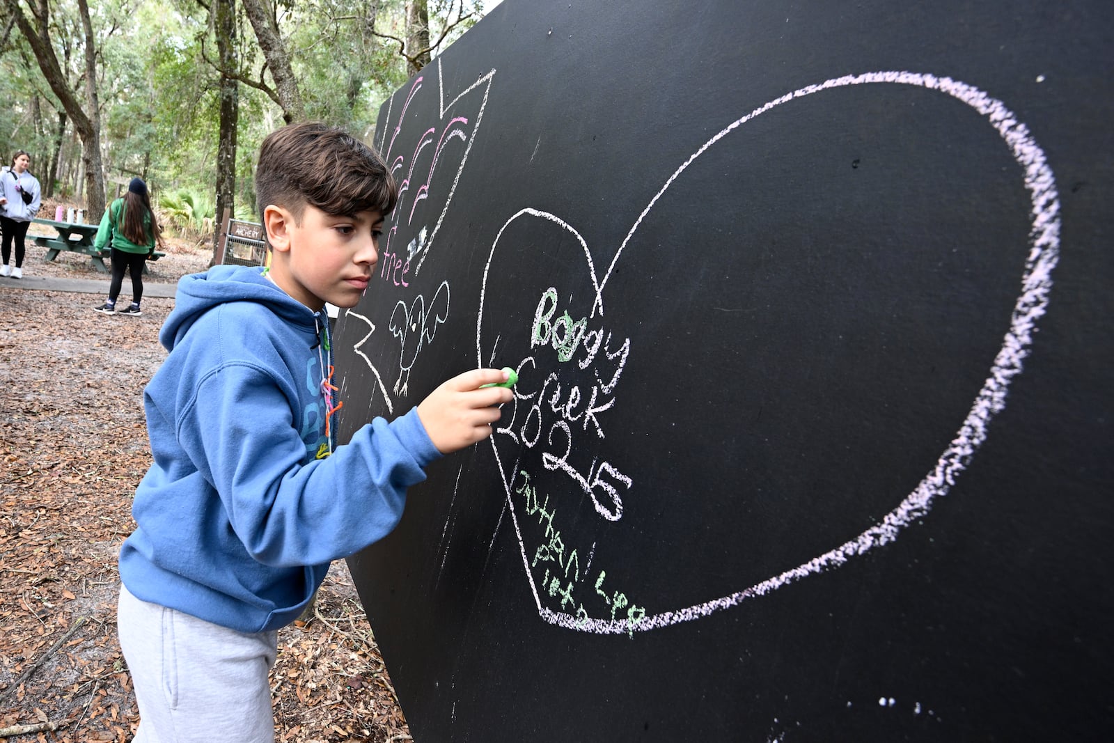 A child writes on a blackboard at Camp Boggy Creek, where children with serious illnesses and their families are provided with a free camp experience, Saturday, Jan. 11, 2025, in Eustis, Fla. (AP Photo/Phelan M. Ebenhack)