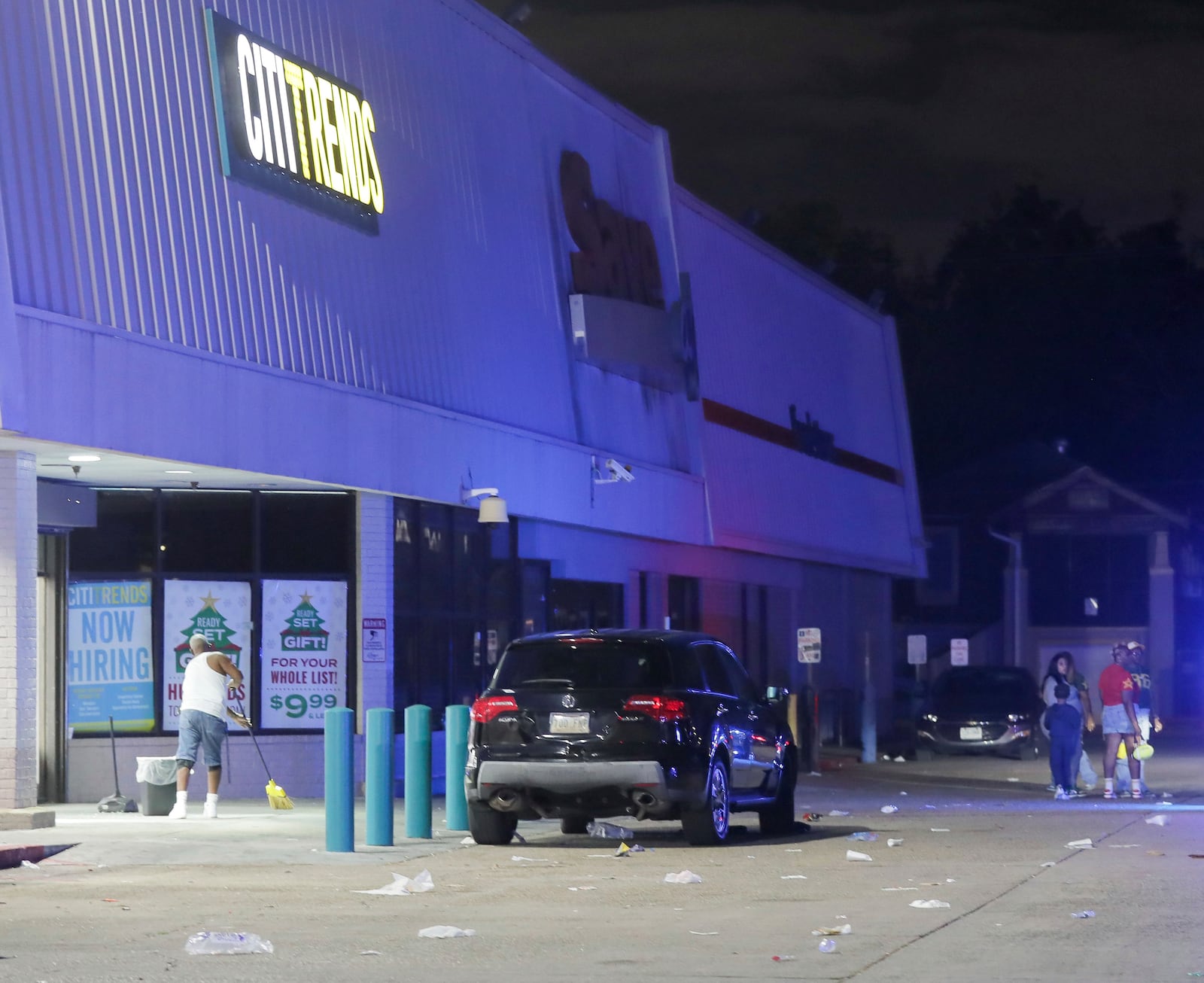 An employee with Cititrends sweeps the ground at a Save O Lot parking lot where several people were shot and killed in New Orleans, Sunday Nov. 17, 2024. (David Grunfeld/The Times-Picayune/The New Orleans Advocate via AP)