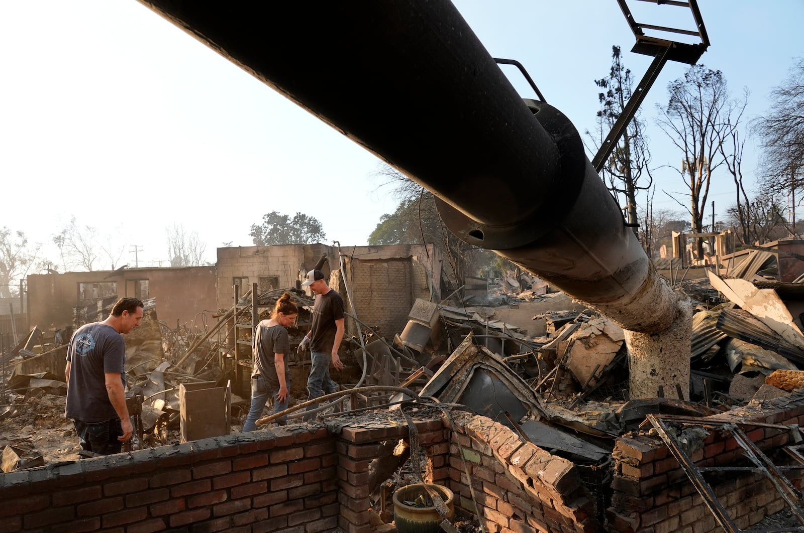 From left, Rob Ramsey, Christina Larson and Larson's husband Chris, the co-owner of the Rancho Bar, look through the ruins of the Rancho Bar a day after it was destroyed by the Eaton Fire, Thursday, Jan. 9, 2025, in Altadena, Calif. (AP Photo/Chris Pizzello)