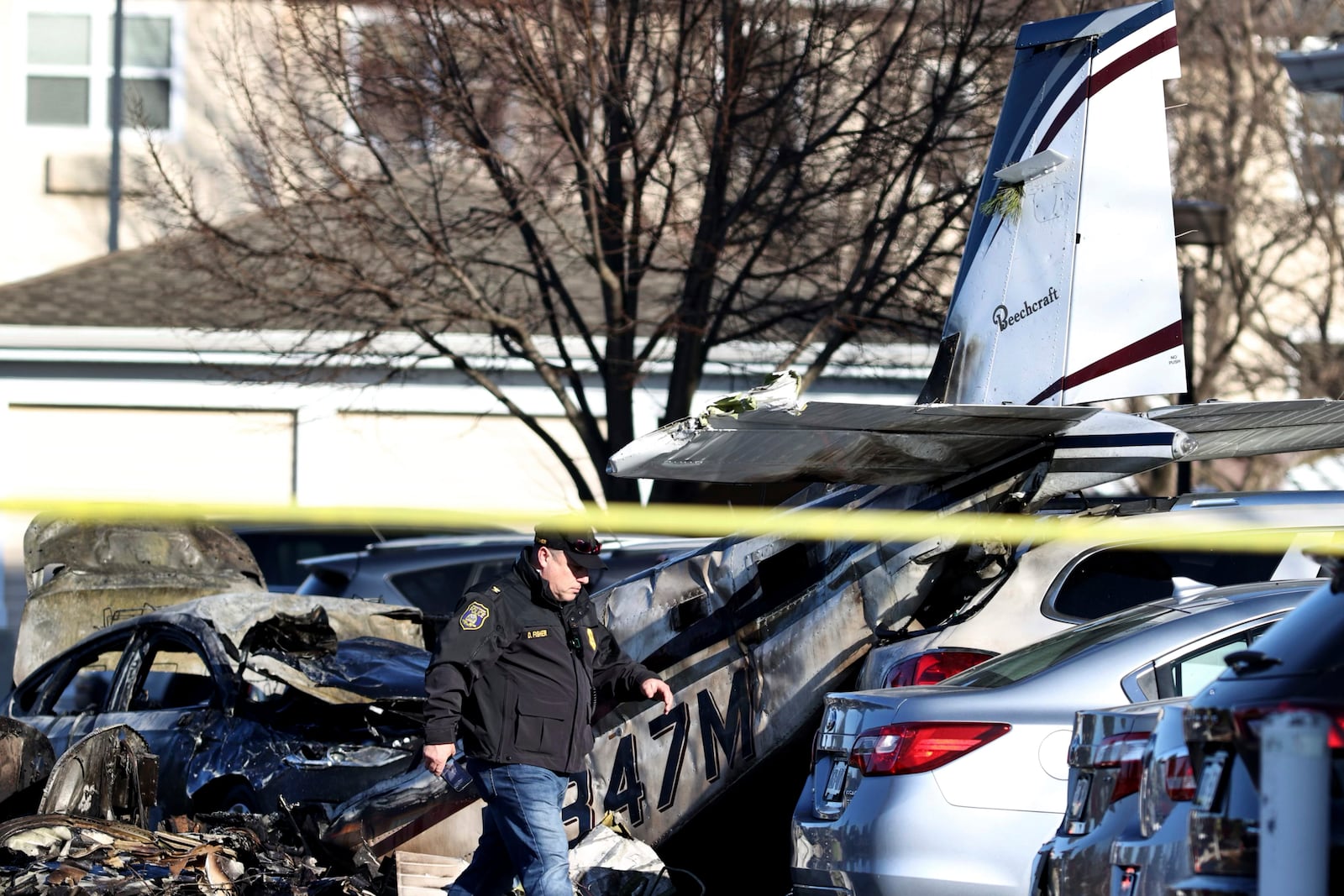 A police officer walks past debris after a plane crashed in a parking lot of a retirement community Sunday, March 9, 2025, in Manheim Township, Pa. (Zach Gleiter/The Patriot-News via AP)