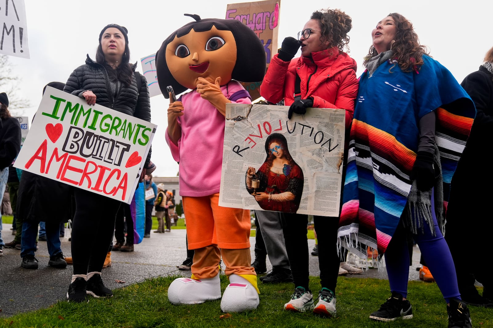 A person in a Dora the Explorer costume stands with Stephanie Snyder, left, Yesenia Celestino, third from left, and Carla Moreno, right, as people gather to protest against the Trump administration and Project 2025 near the Washington State Capitol building Wednesday, Feb. 5, 2025, in Olympia, Wash. (AP Photo/Lindsey Wasson)