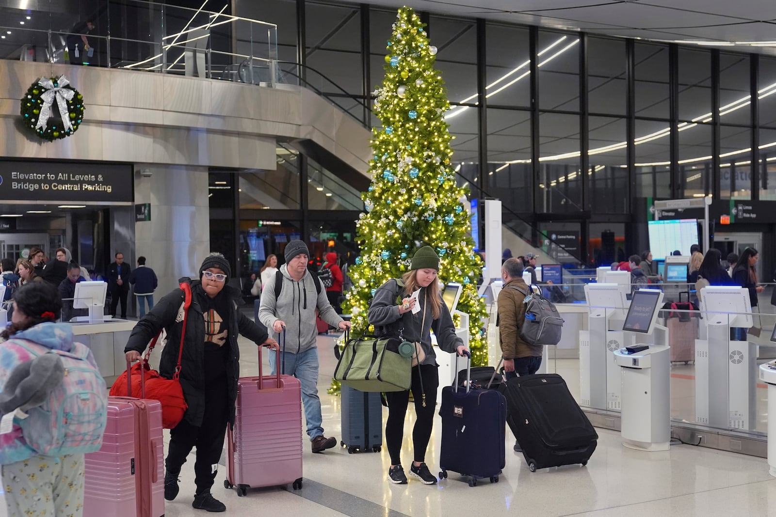 Holiday travelers pass a Christmas tree at Logan Airport, Friday, Dec. 20, 2024, in Boston. (AP Photo/Charles Krupa)