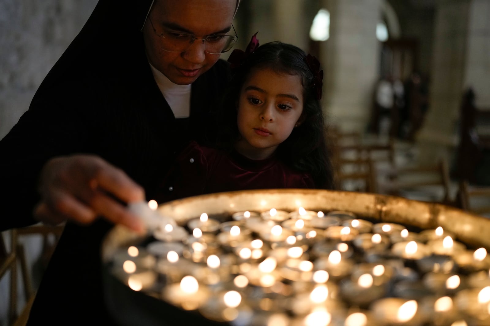 A nun holds a child to light a candle before the Christmas morning Mass at the Chapel of Saint Catherine, traditionally believed to be the birthplace of Jesus, in the West Bank city of Bethlehem, Wednesday, Dec. 25, 2024. (AP Photo/Matias Delacroix)