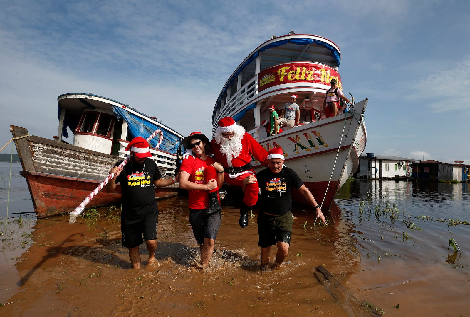 Jorge Barroso, dressed as Santa Claus, is carried by his helpers after arriving on a boat to distribute Christmas gifts to children who live in the riverside communities of the Amazon, in Iranduba, Brazil, Saturday, Dec. 21, 2024. (AP Photo/Edmar Barros)