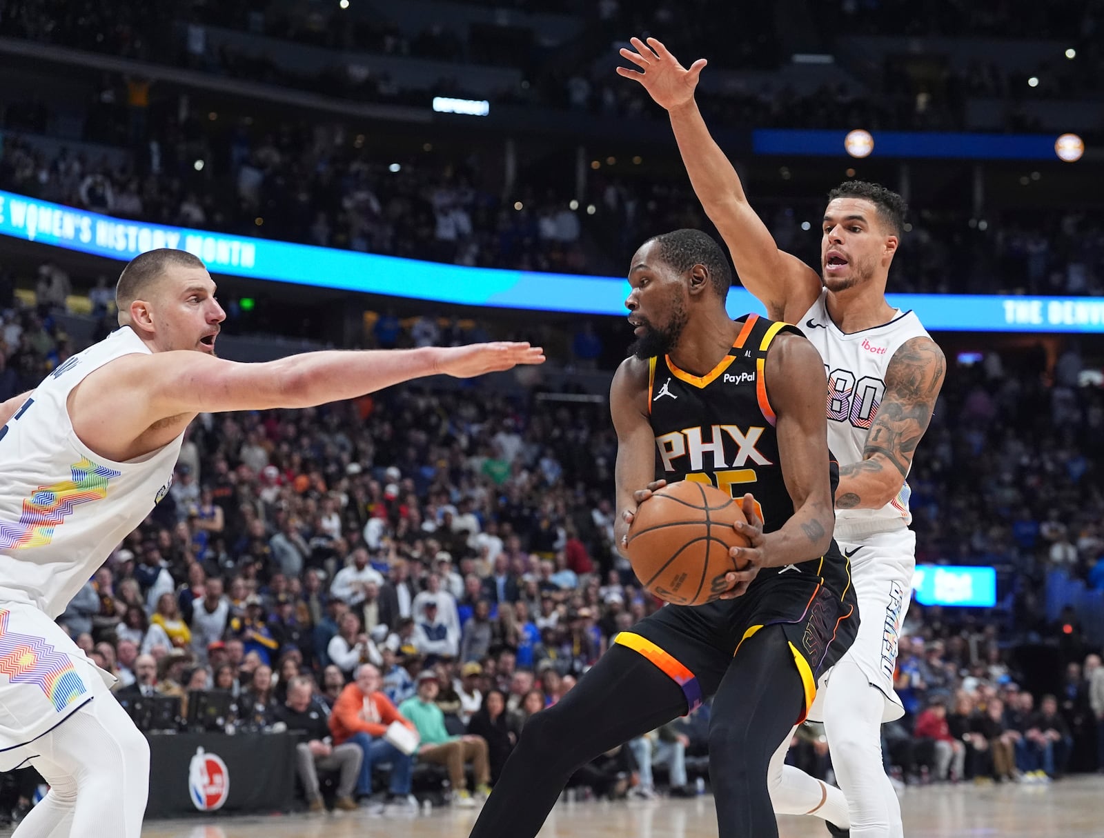 Phoenix Suns forward Kevin Durant, center, passes the ball as Denver Nuggets center Nikola Jokic, left, and forward Michael Porter Jr. defend in overtime of an NBA basketball game Friday, March 7, 2025, in Denver. (AP Photo/David Zalubowski)