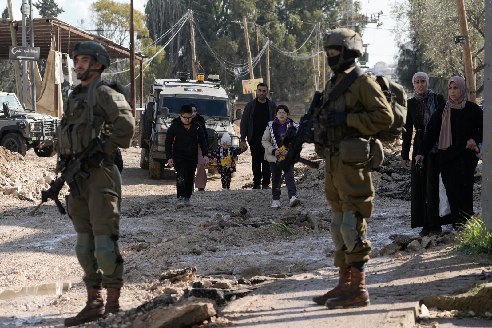 Israeli soldiers stand guard as Palestinians displaced by an Israeli military operation evacuate from the Jenin refugee camp in the West Bank carry their belongings, Thursday, Jan. 23, 2025. (AP Photo/Majdi Mohammed)