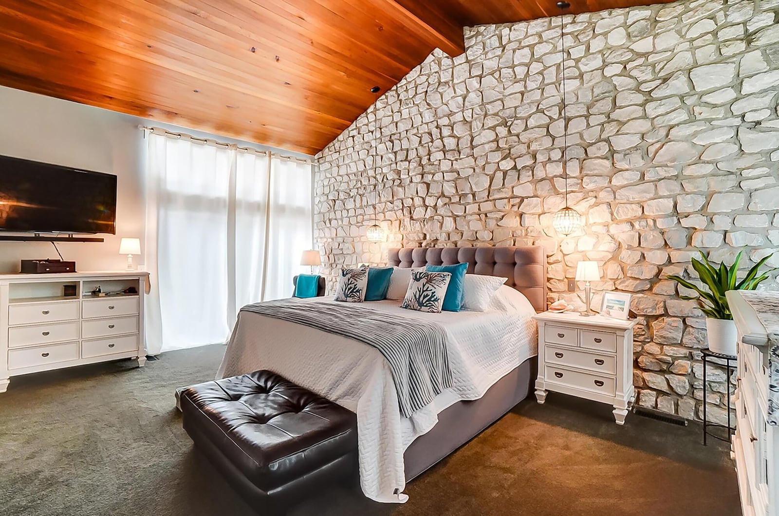 The primary suite is on the second level and has a sliding glass door leading to a private patio with railings. It also has a vaulted wood beamed ceiling and a stone accent wall.