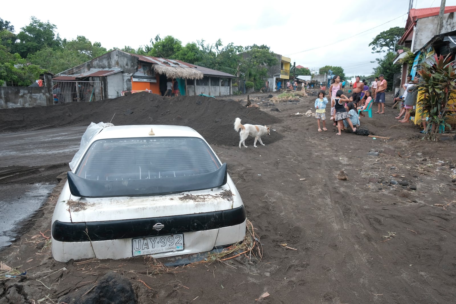 Residents stay beside a car partially buried by volcanic mud that had flowed down from Mayon volcano after heavy rains caused by Tropical Storm Trami hit Guinobatan town, Albay province, Philippines on Wednesday Oct. 23, 2024. (AP Photo/John Michael Magdasoc)