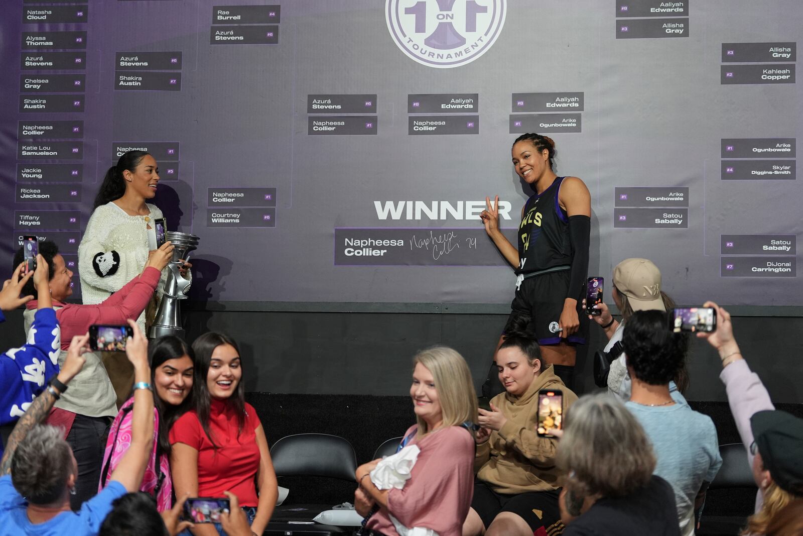 Fans take pictures as Napheesa Collier celebrates next to the tournament bracket, after defeating Aaliyah Edwards in the Unrivaled 1-on-1 basketball final, in Friday, Feb. 14, 2025, in Medley, Fla. (AP Photo/Rebecca Blackwell)