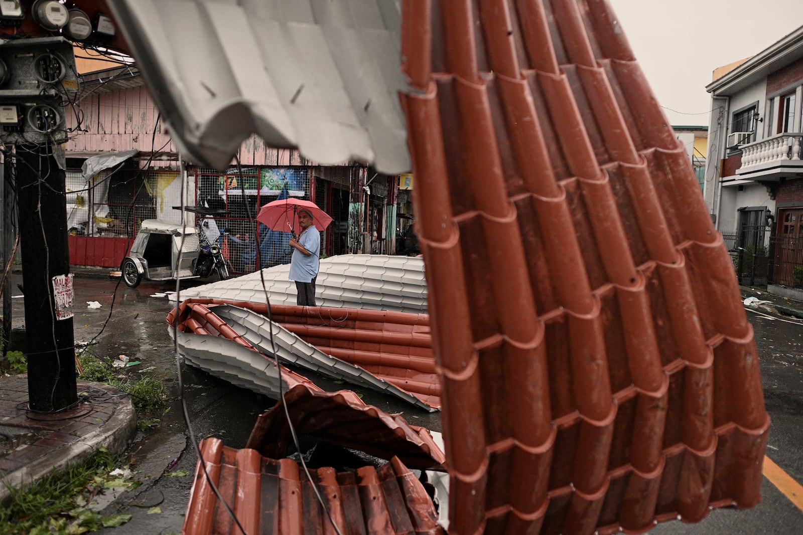 A man walks past roof sheets suspended on electric wires blown by strong winds caused by Typhoon Man-yi along a street in the municipality of Baler, Aurora province, northeastern Philippines, Monday, Nov. 18, 2024. (AP Photo/Noel Celis)