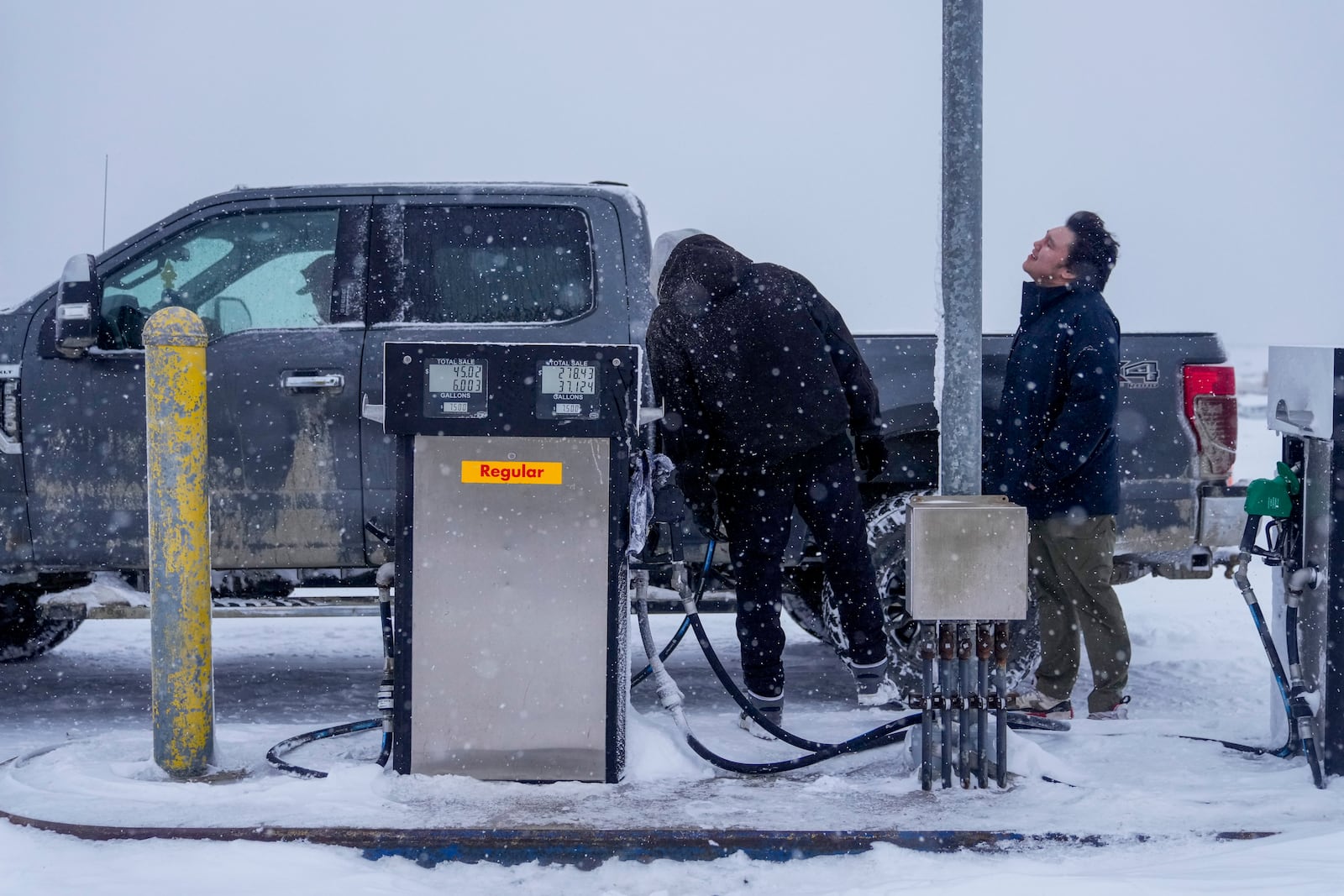 FILE- Edwin Solomon, 18, at right, stands in the wind and snow while filling up a truck with regular gas at a price of $7.50 a gallon, Wednesday, Oct. 16, 2024, in Kaktovik, Alaska. (AP Photo/Lindsey Wasson, File)