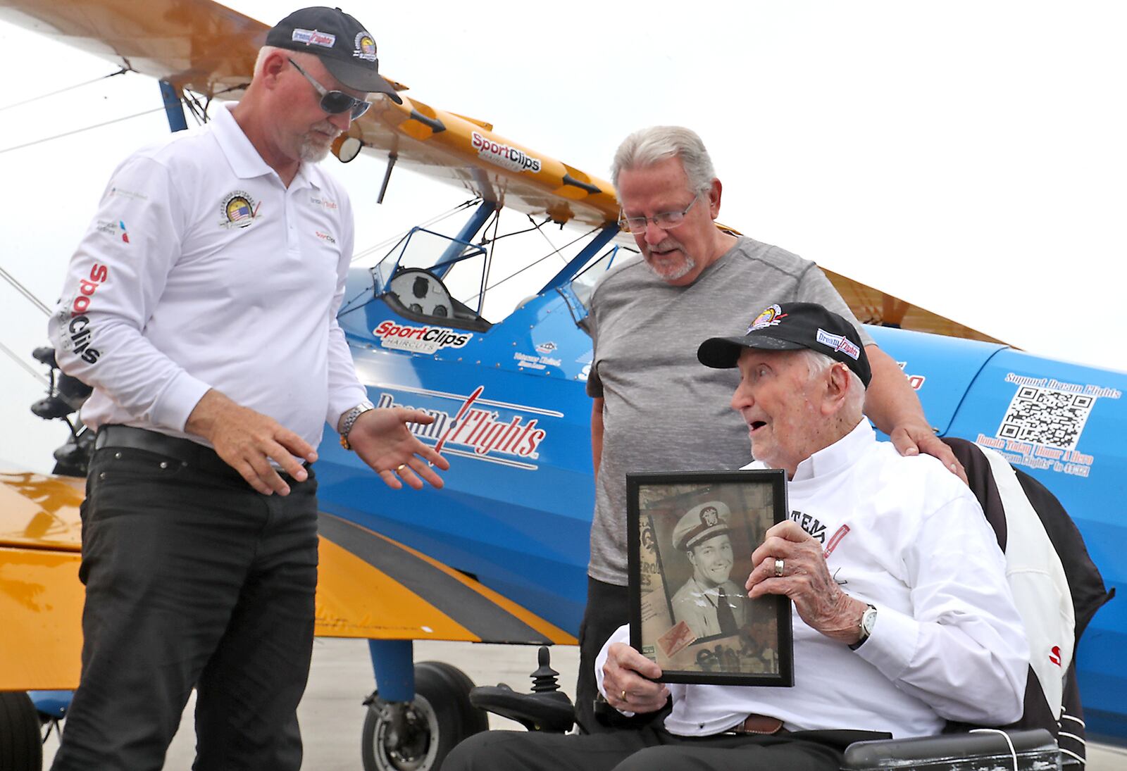 World War II veteran Ed Fisher, who recently turned 100 years-old, shows Ageless Aviation Dreams Foundation pilot Darryl Fisher a picture of himself when he was a pilot in the NAVY Wednesday following his dream flight in a restored Boeing Stearman biplane at Grimes Field in Urbana. Ed's son, Paul, is at his side. BILL LACKEY/STAFF