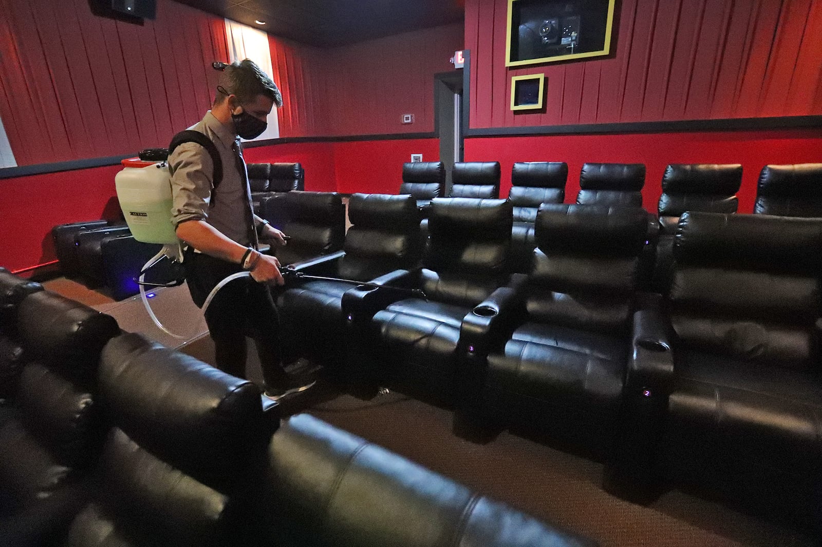 Noah Canter, assistant manager at the UEC Cinema 10 theater in Springfield, sanitizes a theater between shows Friday. Area theaters have been closed for five months. BILL LACKEY/STAFF