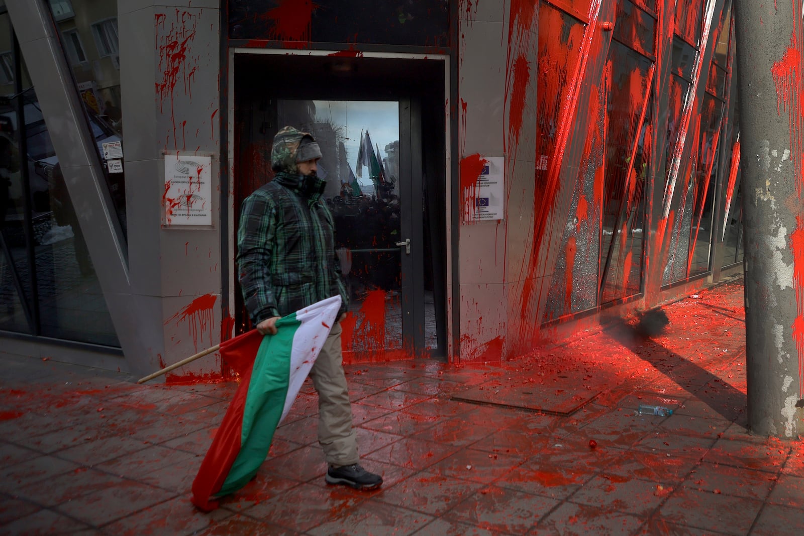 A protester holding Bulgarian flag walks in front of EU commission office in Sofia during nationalist protests demanding the government to scrap plans to take the country into the eurozone, Sofia, Saturday, Feb. 22, 2025. (AP Photo/Valentina Petrova)