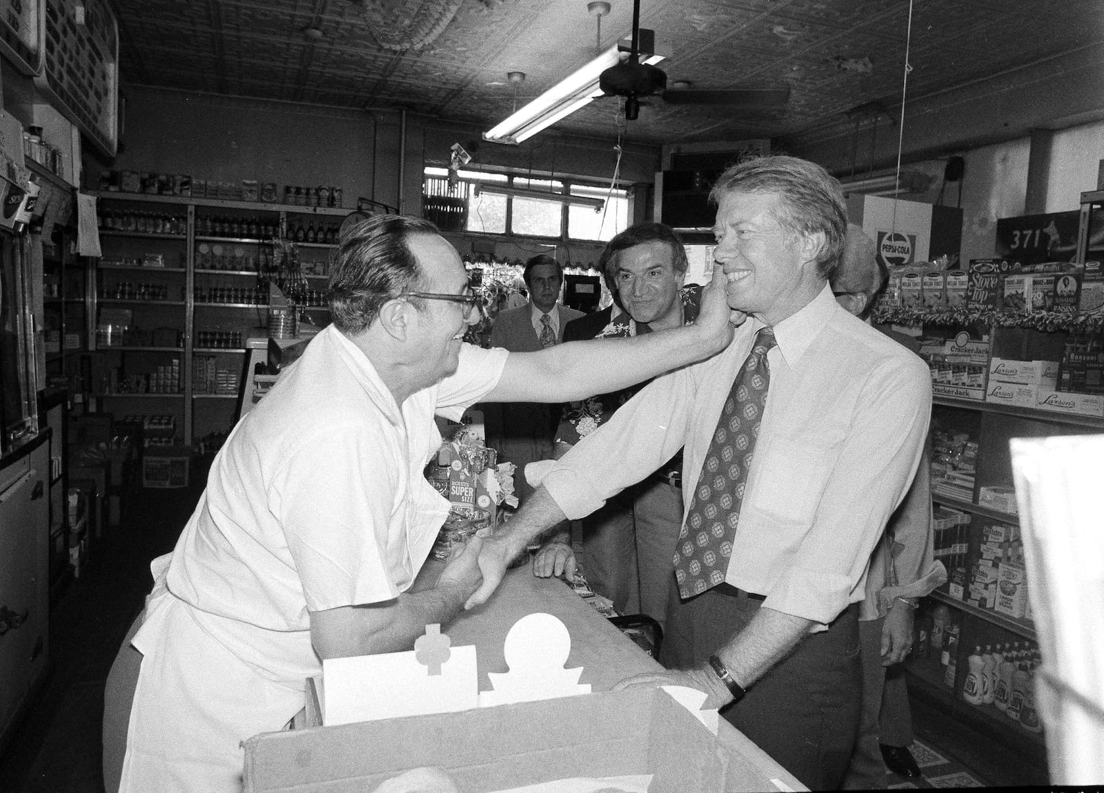 FILE - Democratic presidential candidate Jimmy Carter gets a pinch on the cheek as he greets Charlie Lanzaro, left, at a Queens, N.Y., delicatessen, Aug. 31, 1976. Carter had just arrived in New York on a campaign swing. (AP Photo/Peter Bregg, File)