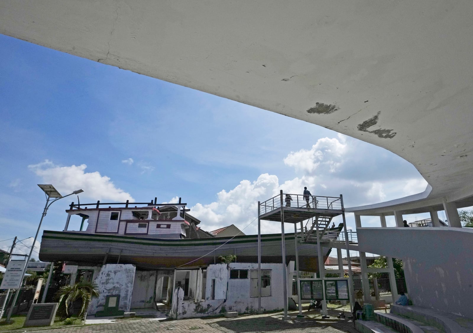 Visitors stand on a platform near a house on which a fishing boat landed after it was swept ashore by the Indian Ocean tsunami in 2004, now preserved as a monument, in Banda Aceh, Indonesia, Friday, Dec. 13, 2024. (AP Photo/Achmad Ibrahim)