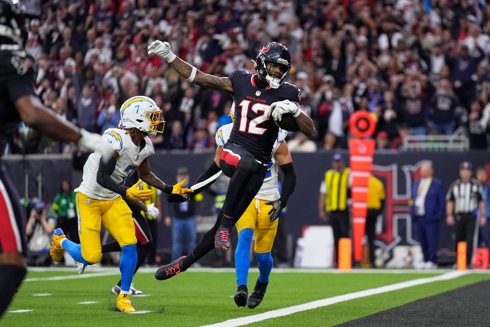 Houston Texans wide receiver Nico Collins (12) leaps into the end zone for a touchdown after catching a pass as Los Angeles Chargers' Kristian Fulton (7) defends during the first half of an NFL wild-card playoff football game Saturday, Jan. 11, 2025, in Houston. (AP Photo/Ashley Landis)