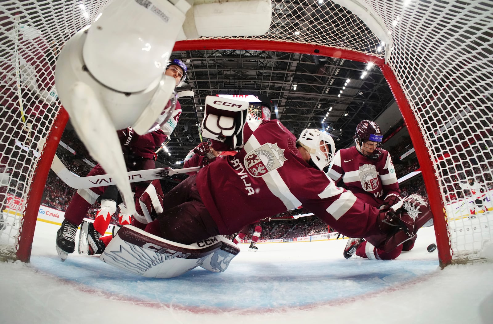 Latvia goaltender Linards Feldbergs, foreground, turns to make a save against Canada with help from teammate Martins Klaucans, right, during first-period IIHF World Junior Hockey Championship preliminary round game action in Ottawa, Ontario, Friday, Dec. 27, 2024. (Sean Kilpatrick/The Canadian Press via AP)