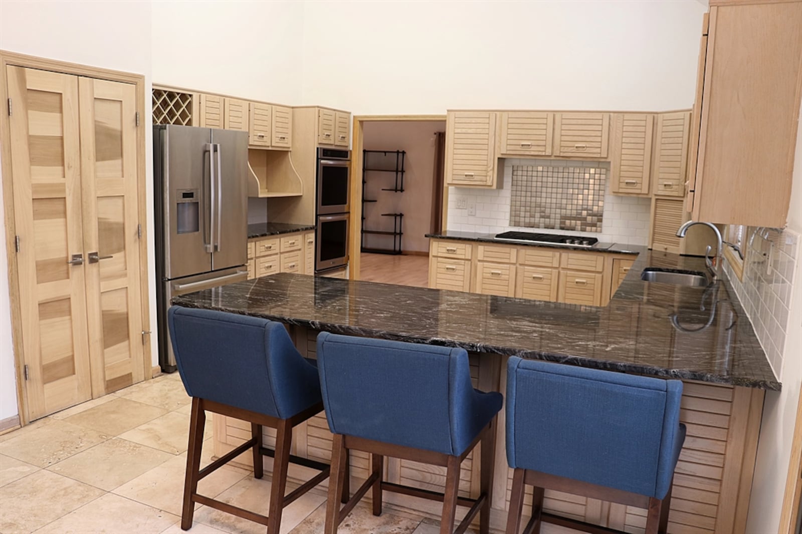 Wood-slat contemporary cabinetry with wood pulls fills the kitchen space and dark granite counters create a U-shaped kitchen space. 