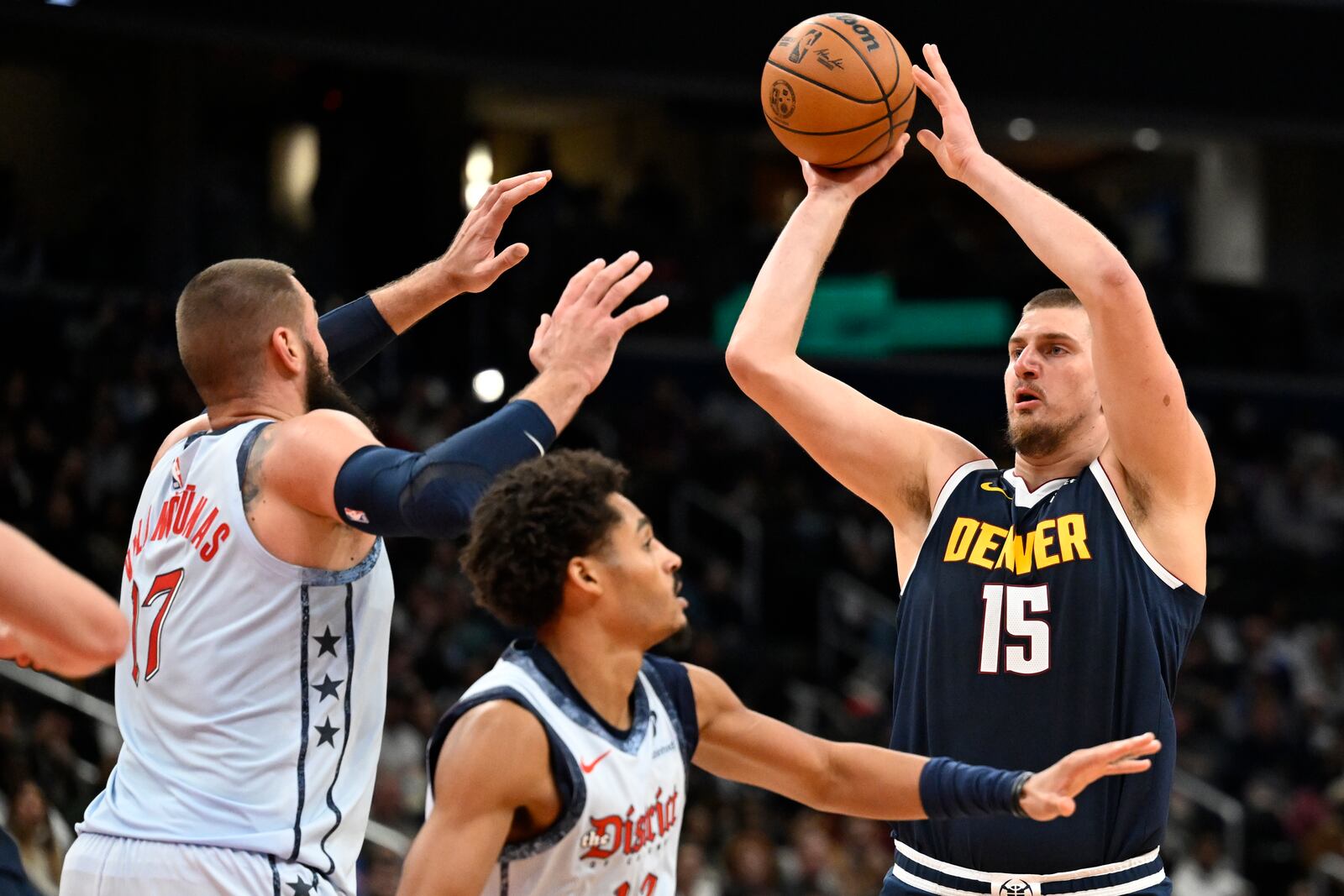 Denver Nuggets center Nikola Jokic (15) loooks to score a basket over Washington Wizards center Jonas Valanciunas, left, and Wizards guard Jordan Poole, center, during the second half of an NBA basketball game Saturday, Dec. 7, 2024, in Washington. (AP Photo/John McDonnell)