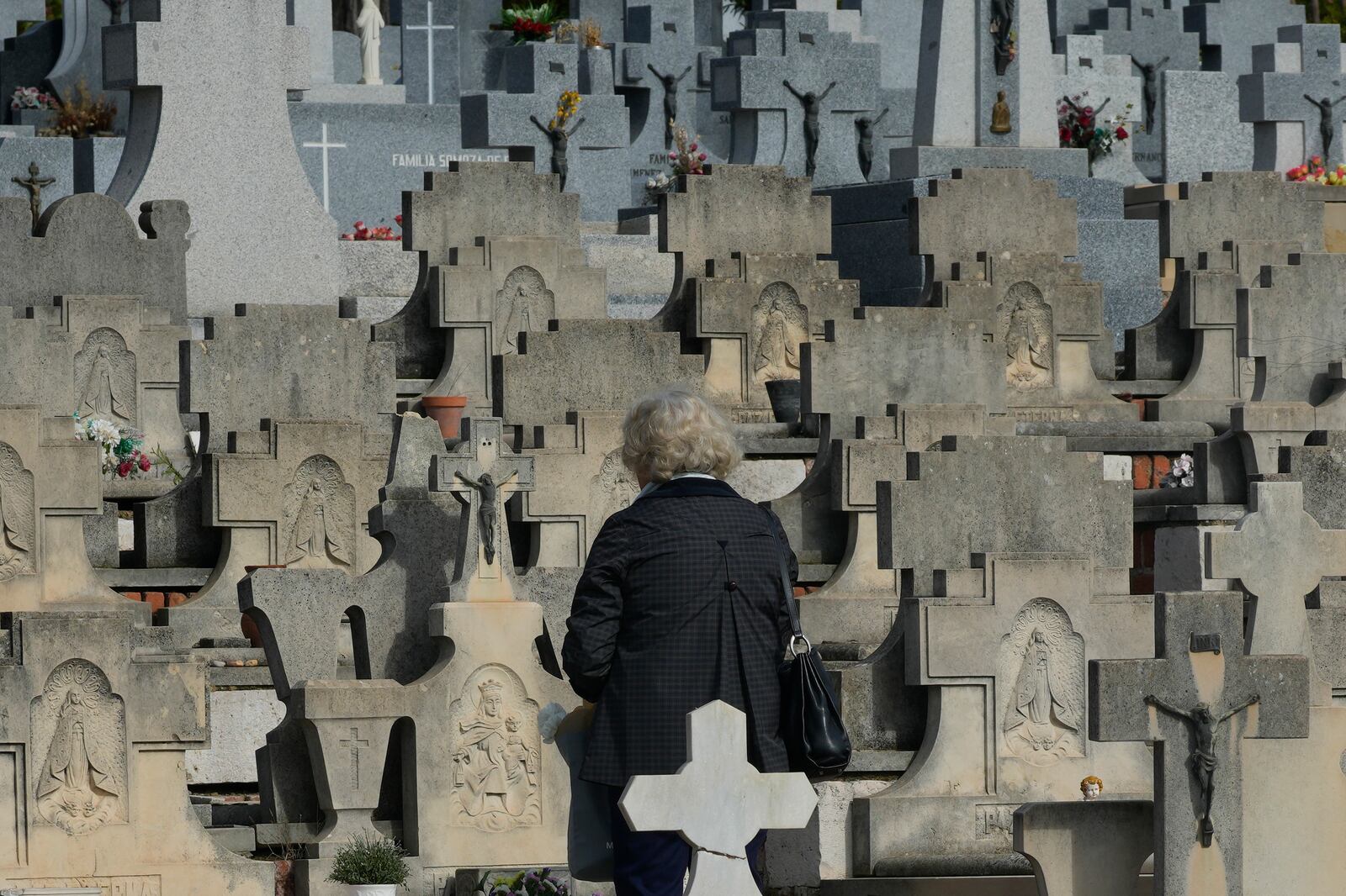 A woman stands in front of a grave in the Almudena cemetery during All Saints Day, a Catholic holiday to reflect on the saints and deceased relatives, Madrid, Spain, Friday, Nov. 1, 2024. (AP Photo/Paul White)