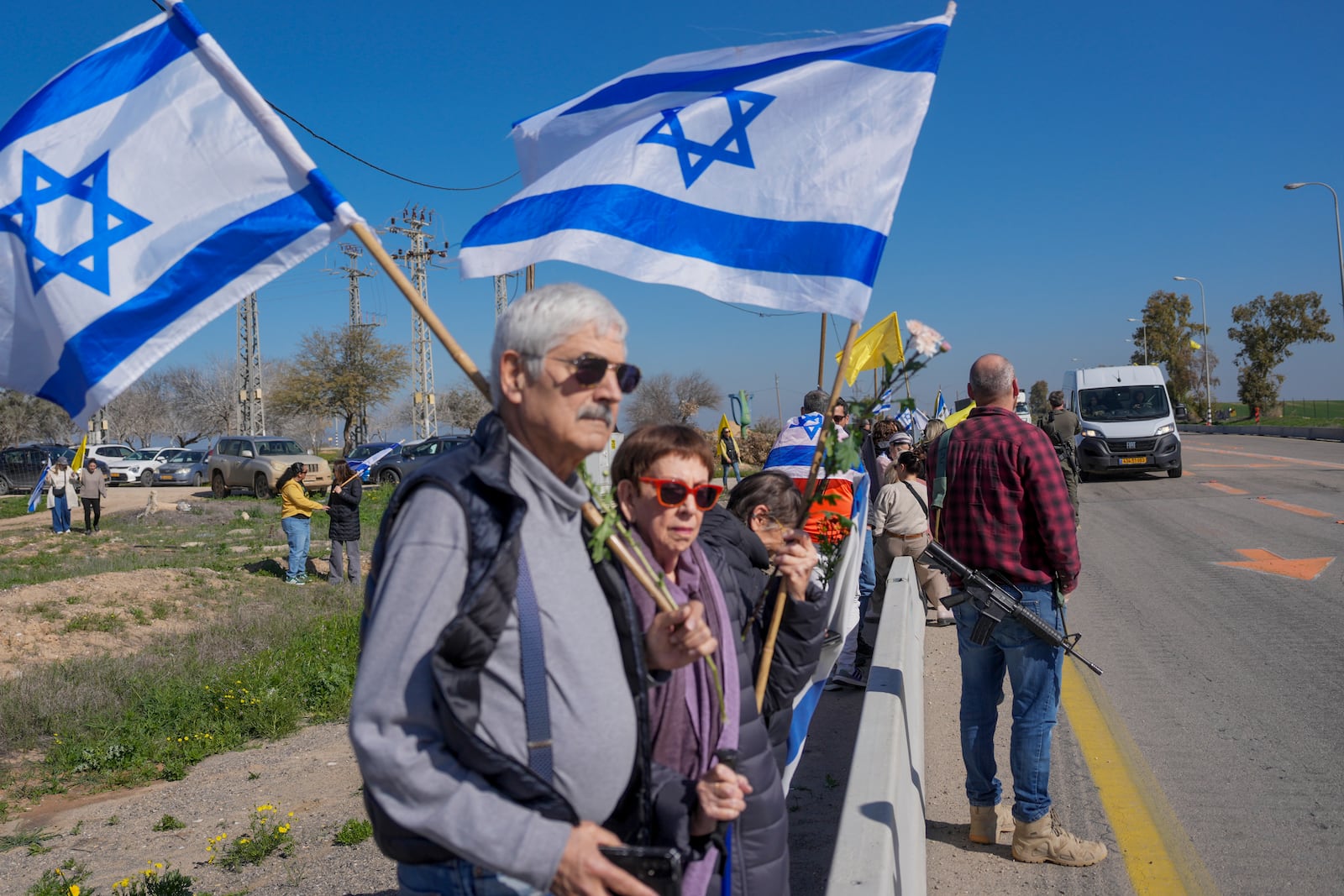 Israelis are waiting on the side of a road where the funeral convoy carrying the coffins of slain hostages Shiri Bibas and her two children, Ariel and Kfir, will pass by near Kibbutz Nir Oz, Israel, Wednesday, Feb. 26, 2025. The mother and her two children were abducted by Hamas on Oct. 7, 2023, and their remains were returned from Gaza to Israel last week as part of a ceasefire agreement with Hamas. (AP Photo/Ohad Zwigenberg)