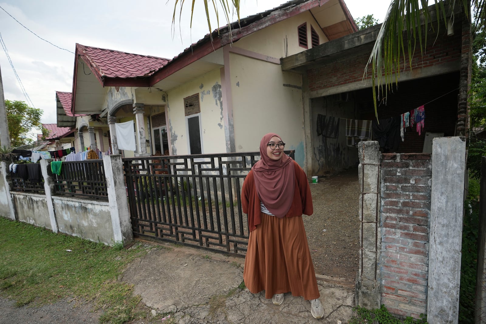 Qurrata Ayuni, a 28-year-old tsunami survivor, stands outside her house, built on the same spot where her parents' home once stood before it was destroyed by the disaster in 2004 in Lampuuk on the outskirts of Banda Aceh, Indonesia, Friday, Dec. 13, 2024. (AP Photo/Achmad Ibrahim)