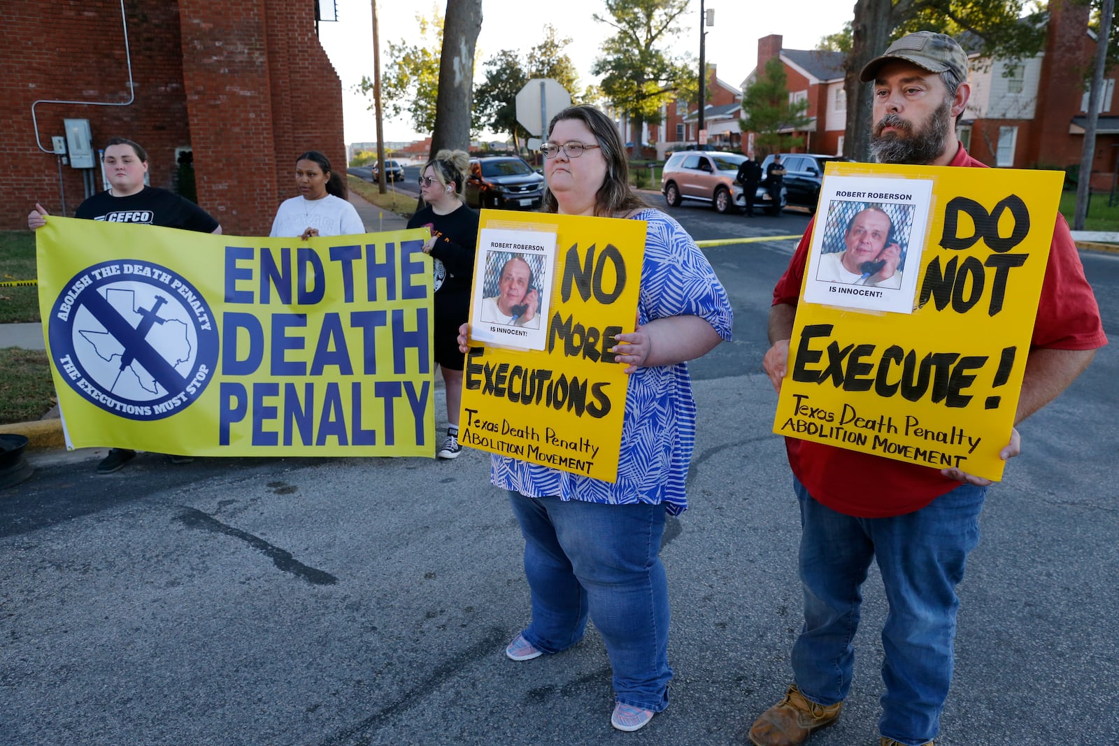 Jennifer Martin, center, and Thomas Roberson, right, older brother of condemned prisoner Robert Roberson, holds signs with others as they protest outside the prison where Roberson is scheduled for execution at the Huntsville Unit of the Texas State Penitentiary, Thursday, Oct. 17, 2024, in Huntsville, Texas. (AP Photo/Michael Wyke)