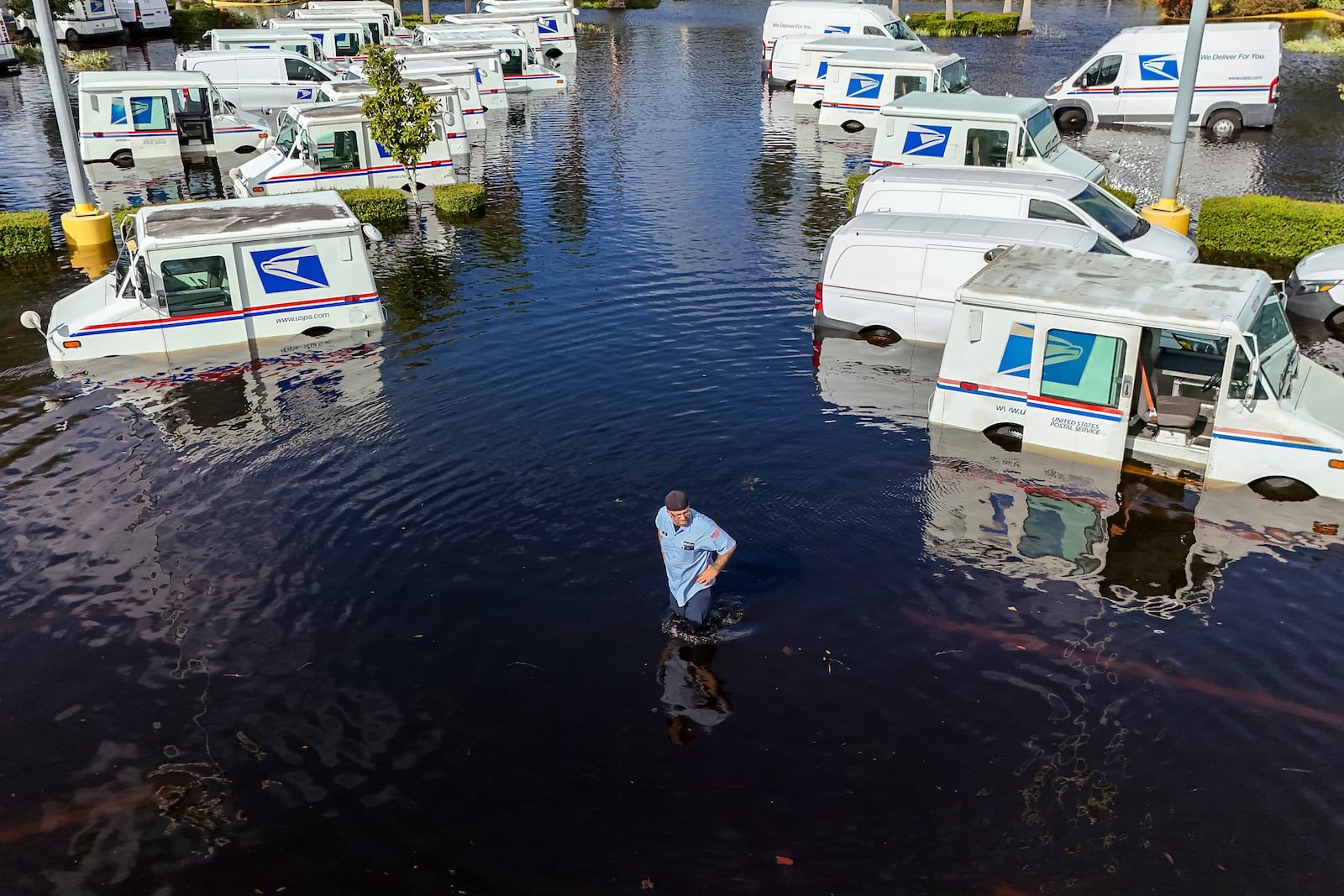 A USPS worker inspects trucks that had been relocated to protect them from wind but which are now underwater as intense rain from Hurricane Milton caused the Anclote River to flood, Friday, Oct. 11, 2024, in New Port Richey, Fla. (AP Photo/Mike Carlson)