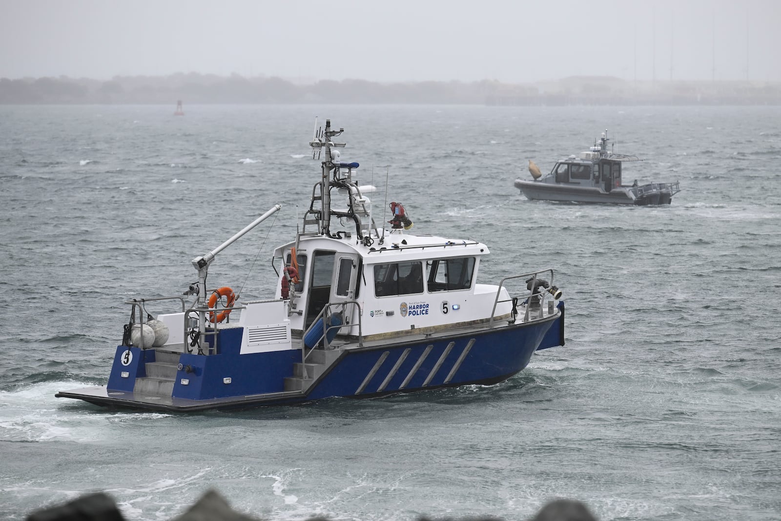 A San Diego Harbor patrol and a U.S. Navy boat work along the shore near Shelter Island after a U.S. Navy plane crashed into the San Diego Bay, Wednesday, Feb. 12, 2025, in San Diego. (AP Photo/Denis Poroy)